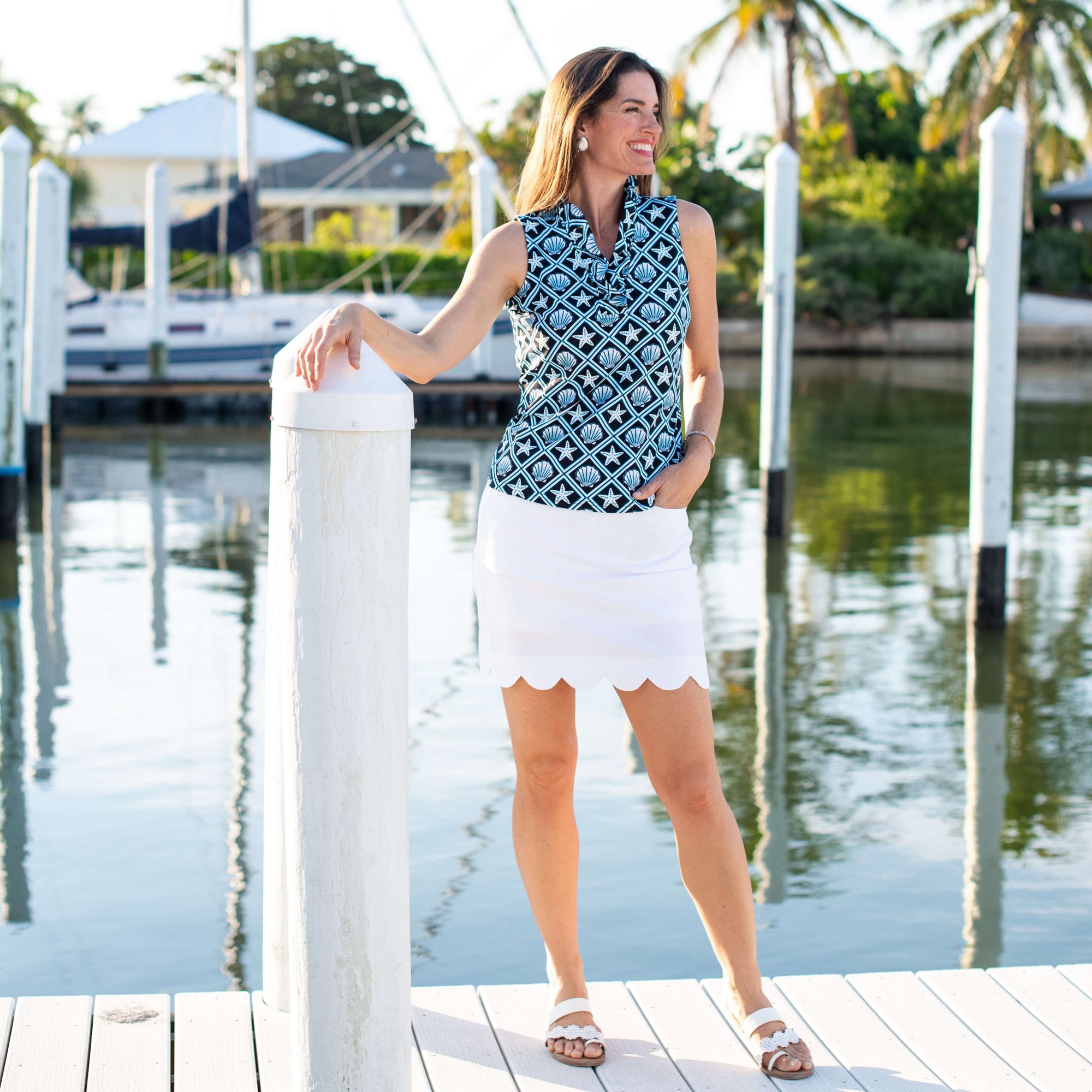 A woman in a sleeveless printed top and white skort leans against a mooring on a dock