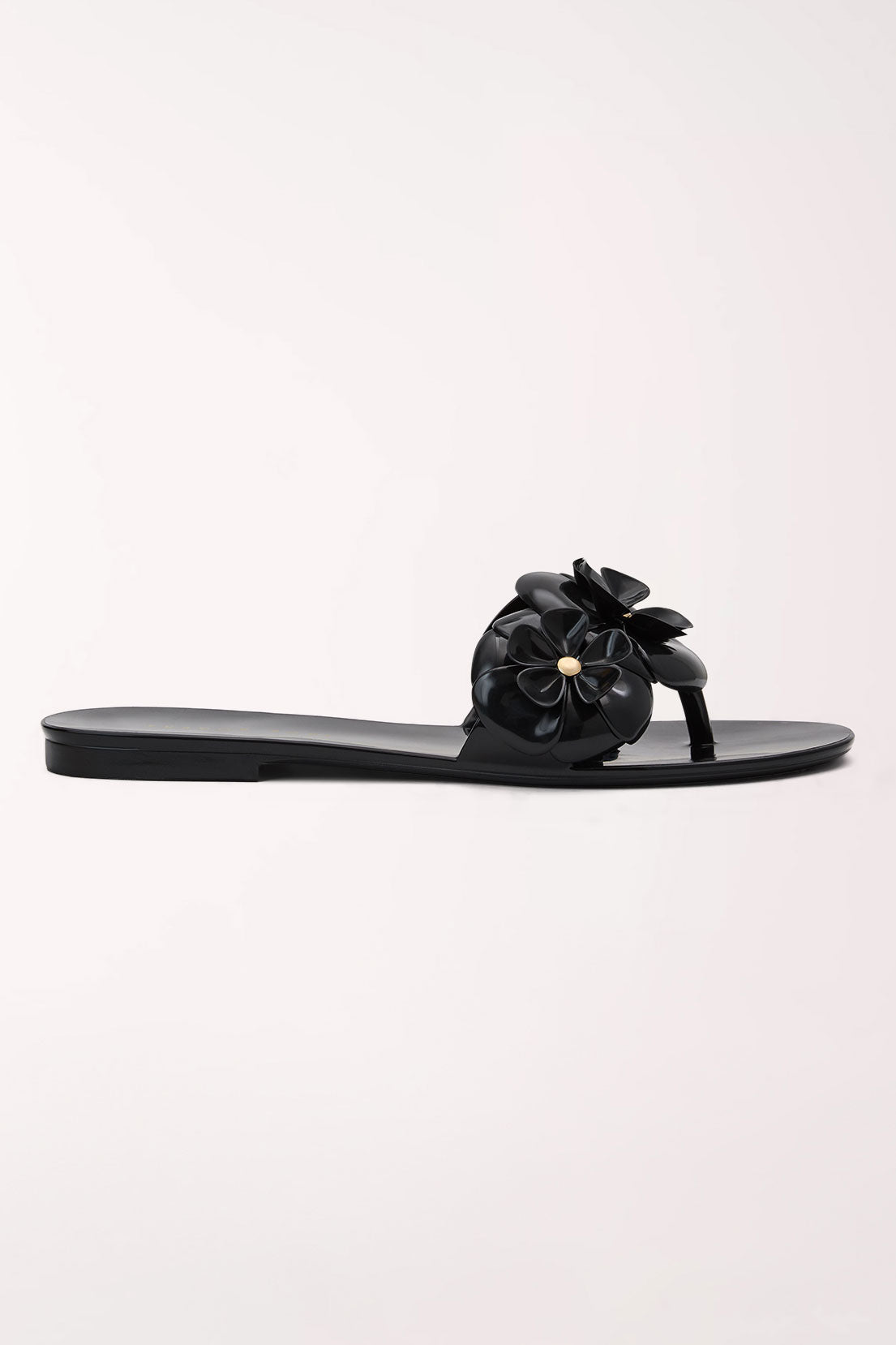 A single black jelly thong sandal with a large, dimensional flower embellishment on the strap, featuring a small gold center detail, shown against a plain off-white background.