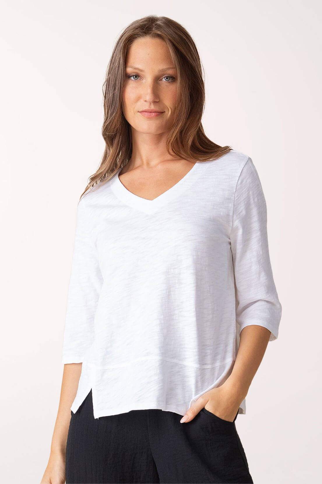 Woman wearing a white V-neck top with black pants on a white background