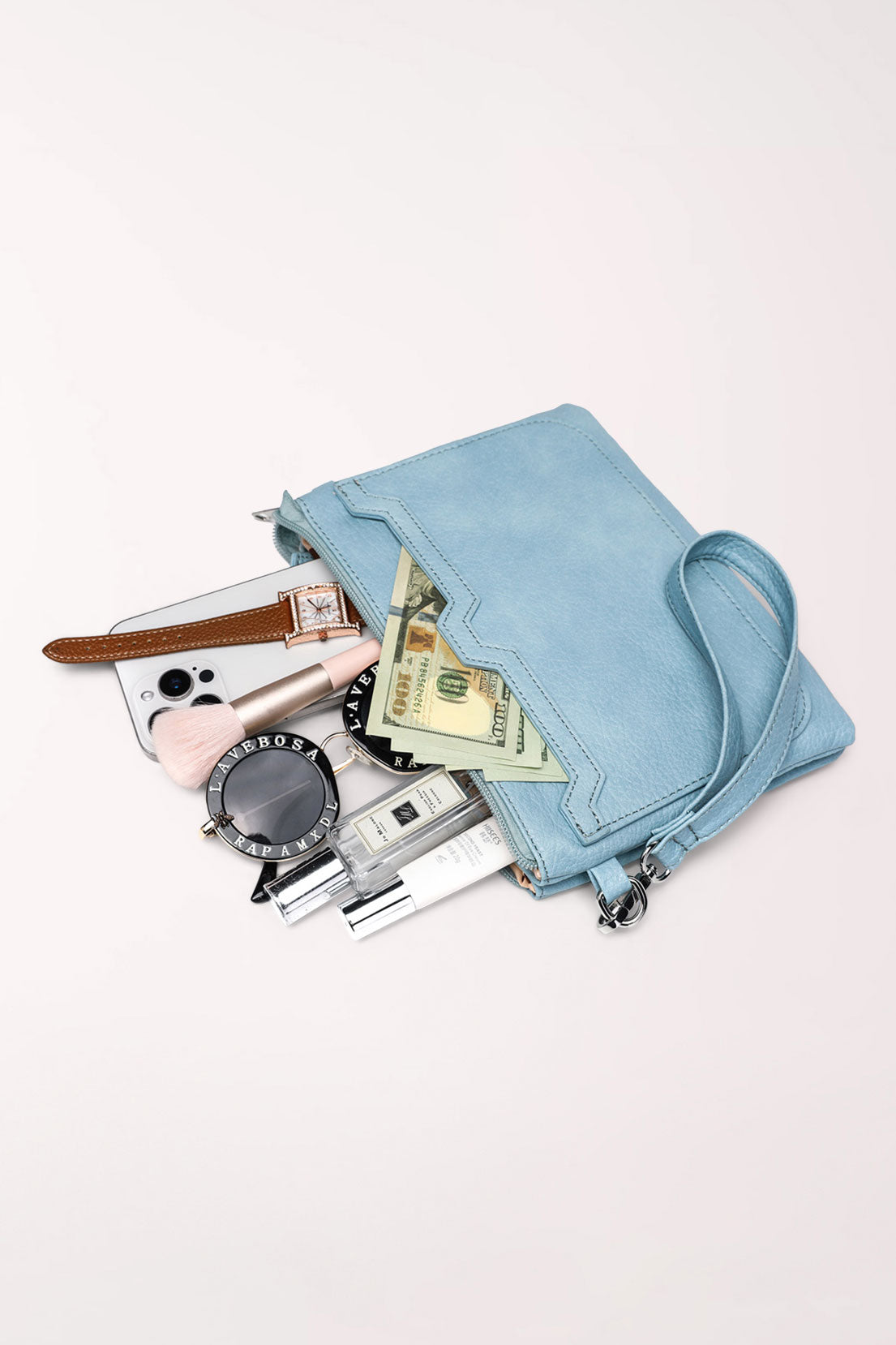 The baby blue 22 Tote Two-Sided Crossbody Bag lying on its side with a phone, cash, watch, sunglasses and makeup spilling out to show what fits inside.