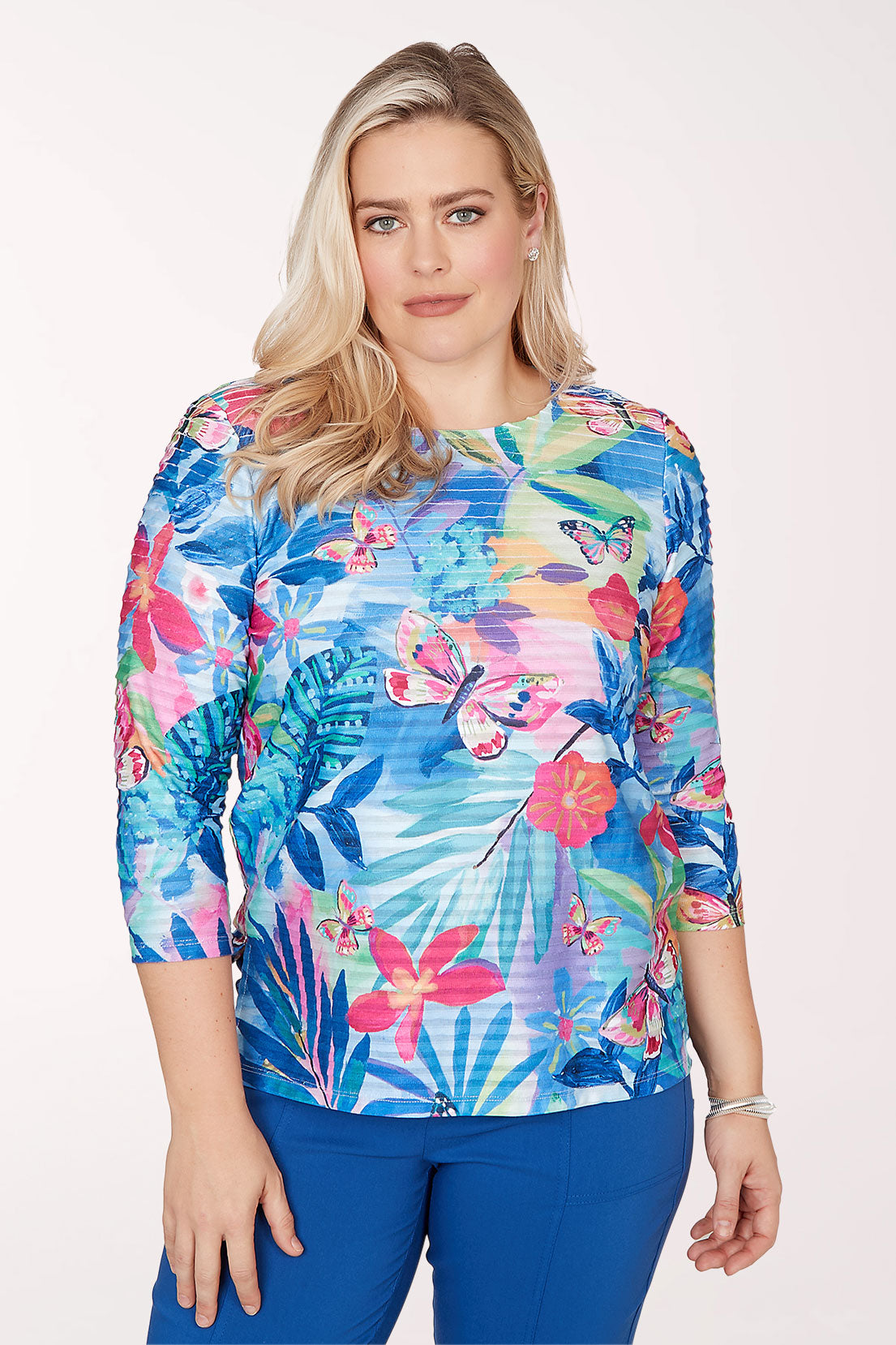 Woman wearing a colorful floral print top with blue pants on a white background