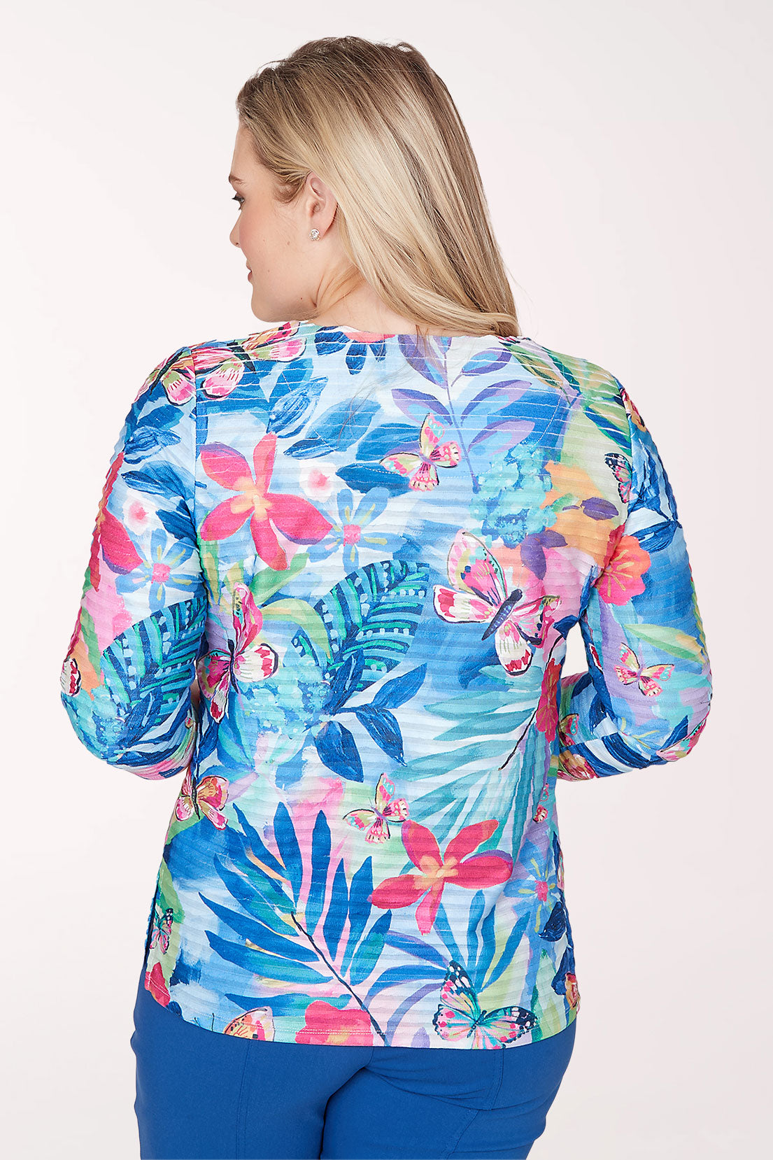 Woman wearing a colorful floral print top with blue pants on a white background