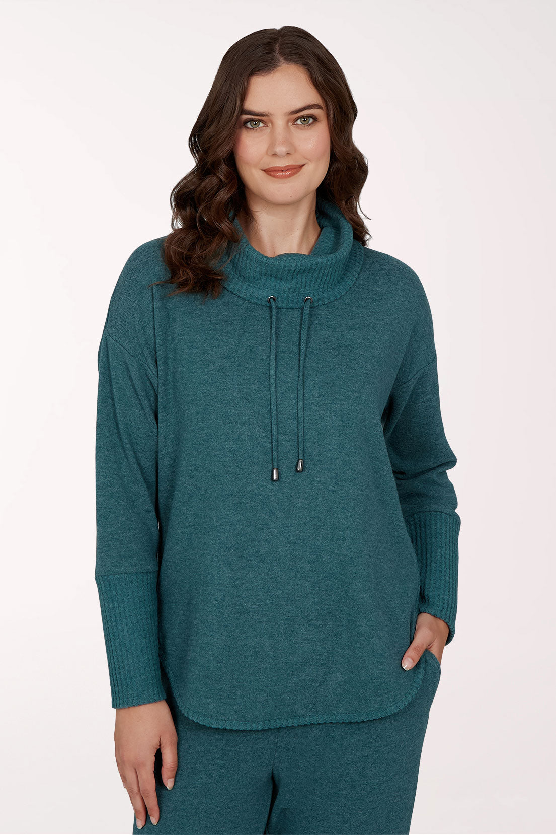 A woman wearing a teal green knit mock neck sweater with a drawstring detail and matching knit pants, photographed against a clean white studio background.