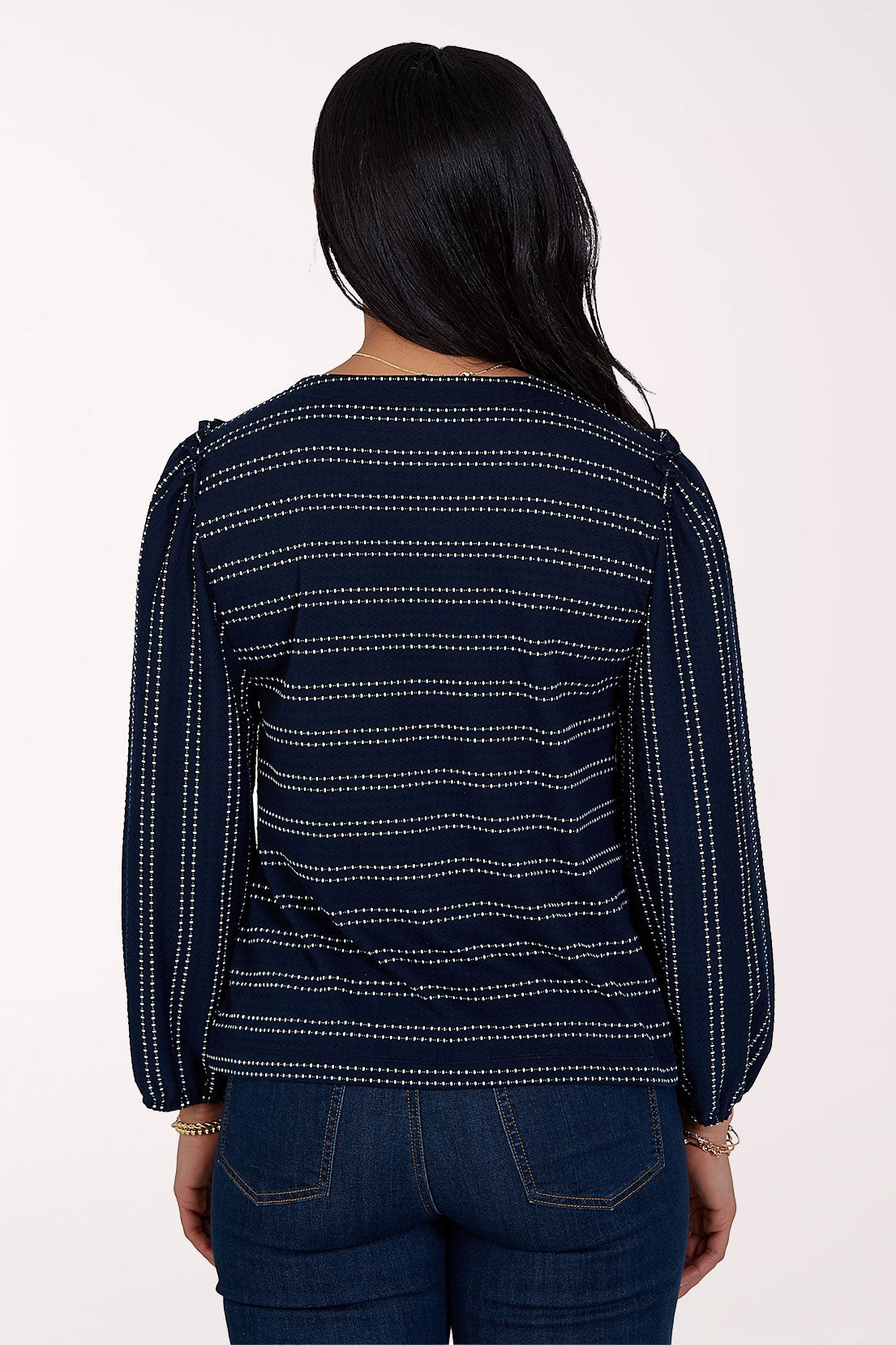 A woman modeling a navy blue long-sleeve top with thin white dotted horizontal stripes, paired with dark blue jeans, against a plain white studio background.