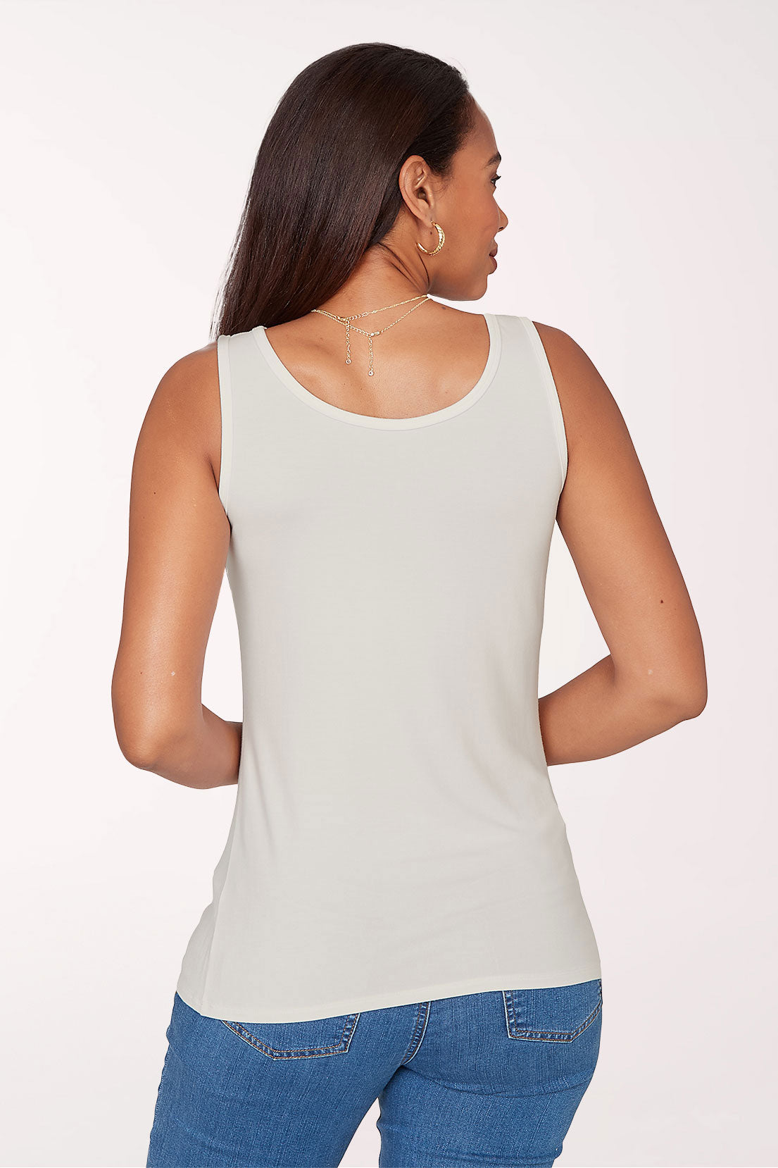 Woman wearing a light gray tank top and blue jeans on a white background