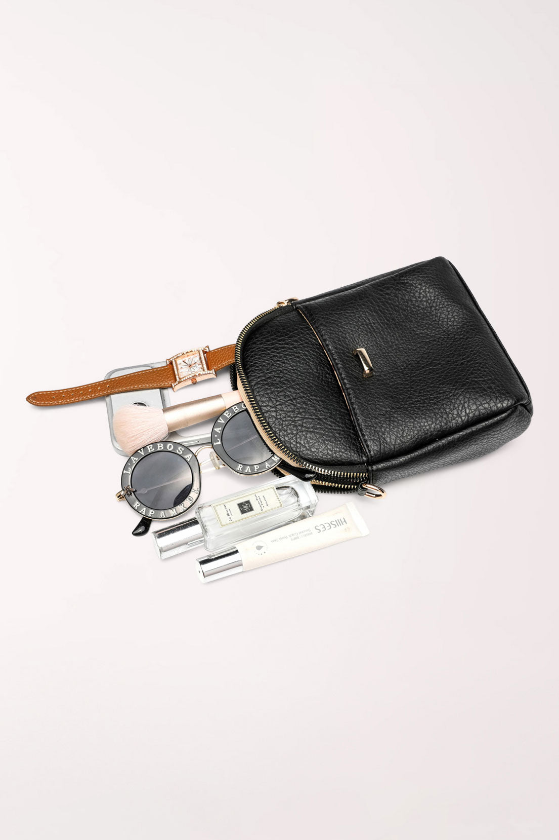 The black 22 Tote Four-Pocket Crossbody Bag lying flat with a watch, sunglasses and perfume beside it to show what fits inside.