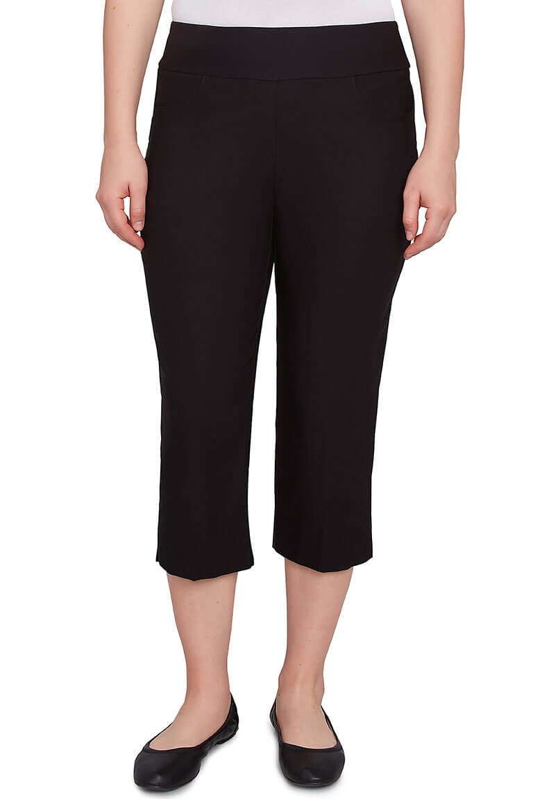 A front shot of a model wearing a black-colored pull-on silky capri pant with an elasticized waistband, dual front and back pockets, and a straight hemline with side slits.