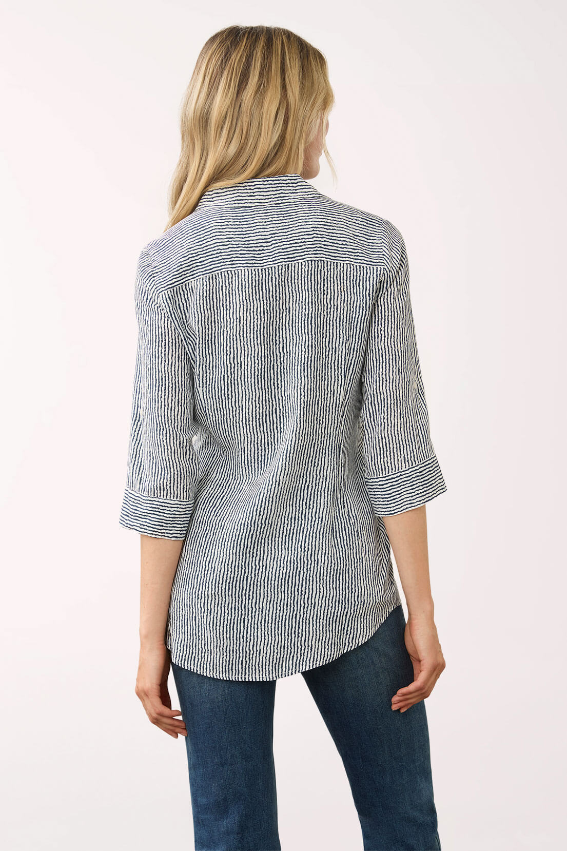 A woman shown from the back wearing a gray and white vertically striped button-down shirt with three-quarter sleeves and blue jeans, set against a plain light background.