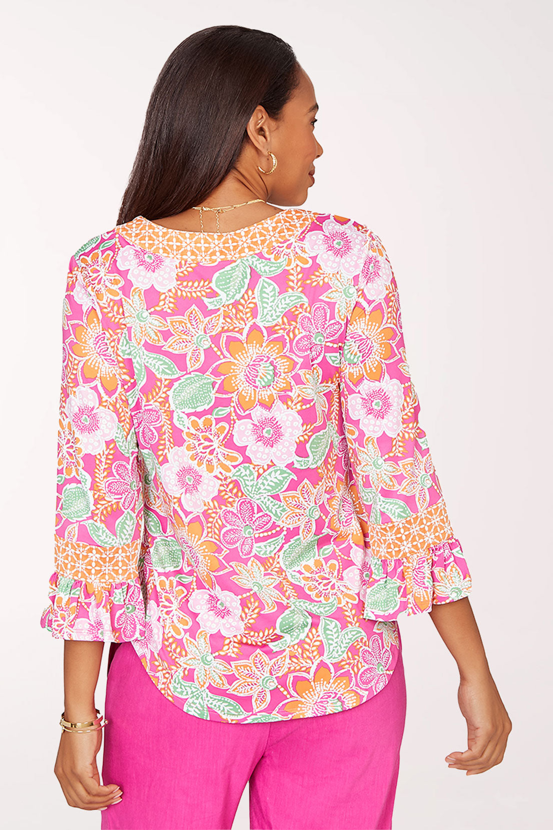 Woman wearing a colorful floral blouse and pink pants on a white background