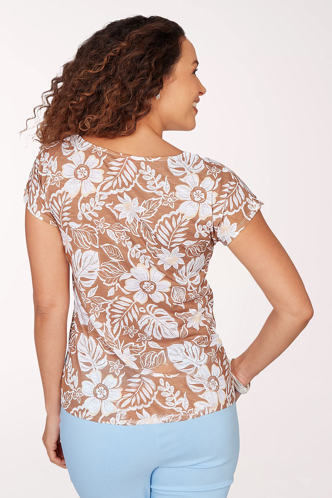 Woman wearing a floral lace top and light blue jeans on a white background