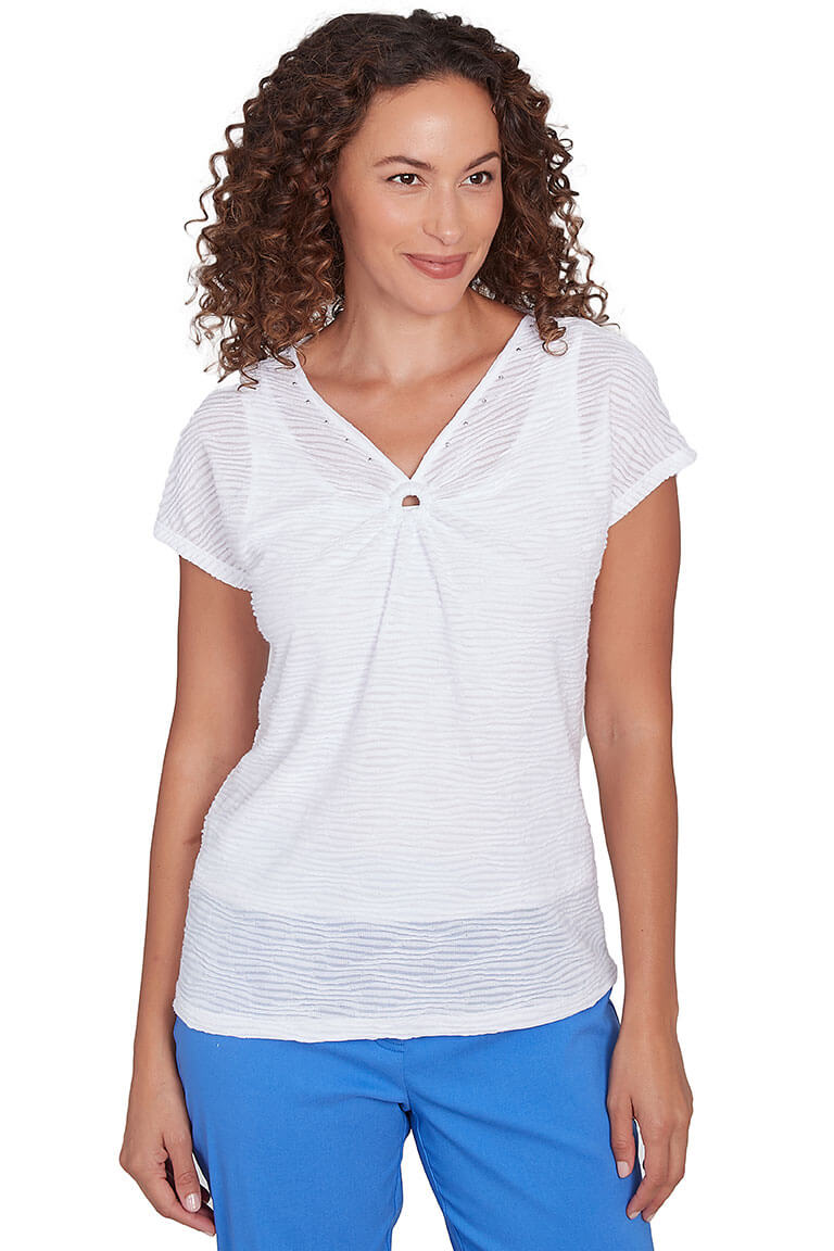 A front shot of a model wearing a white cap sleeve knit top with a V-neckline, ringed styling, and rhinestone studded embellishment. The top has a straight hemline and wave-textured fabric.