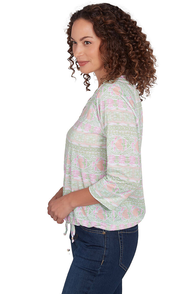 A back shot of a model wearing a green and pink floral top with a lace-up neckline and 3/4 raglan sleeves.
