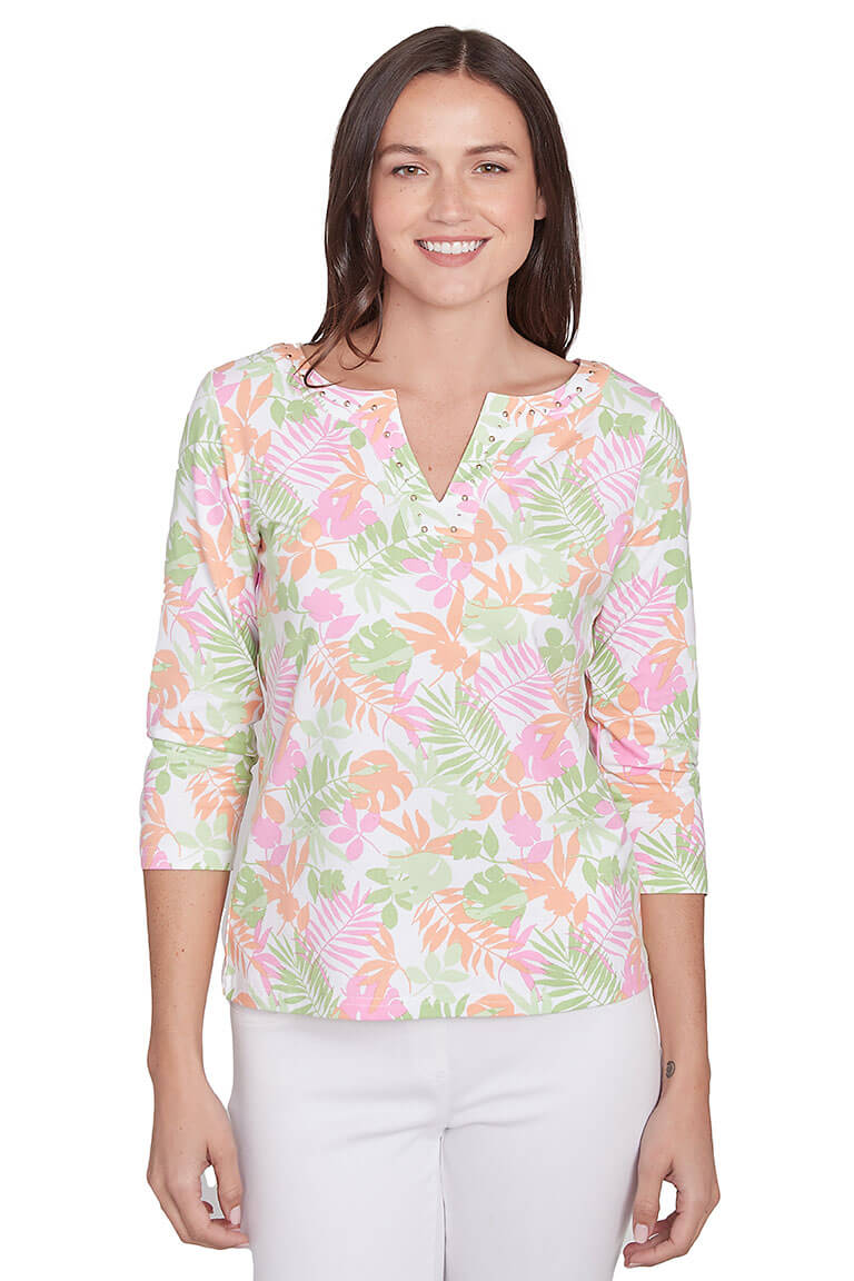 A front shot of a model wearing a floral print pink and green 3/4 sleeve top with a notched v-neckline and studded embellishment, paired with white pants.