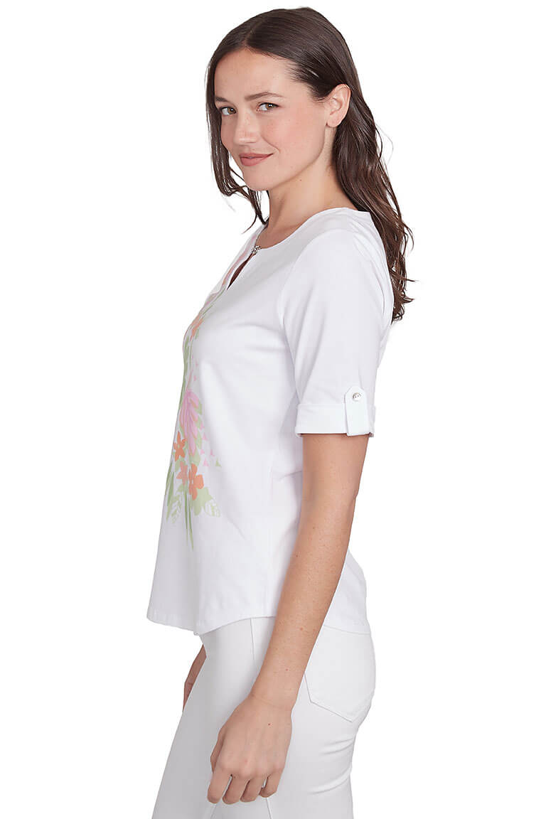 A side shot of a model wearing a white top with tropical leaf prints and short sleeves. The top features a notched neck and metallic closure on the neckline.