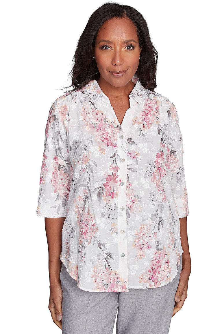 A woman wearing a white, pink, and green floral button-front jacquard blouse with a foldover collar, pleated shoulders, and 3/4 sleeves with slits on the cuffs.