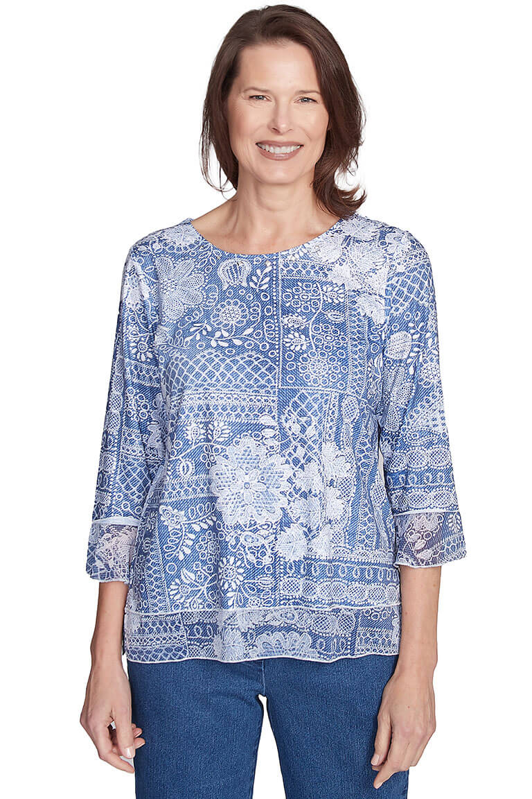 A woman wearing a blue and white paisley printed scoop neck knit top with 3/4 sleeves and chiffon flounce cuffs, rhinestone embellishment on neckline, and a straight hemline with side slits.