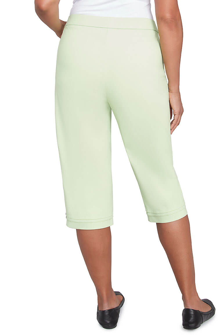 A back shot of a pair of parrot green pleated hem capri pants with a stretch waistband, dual front pockets, and button detail on the hemline.