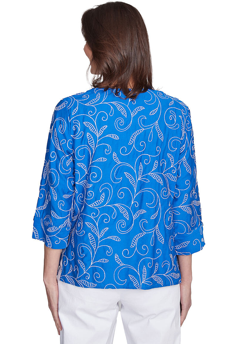 A back shot of a woman wearing a blue v-neck blouse with 3/4 sleeves and all-over embroidered embellishment.