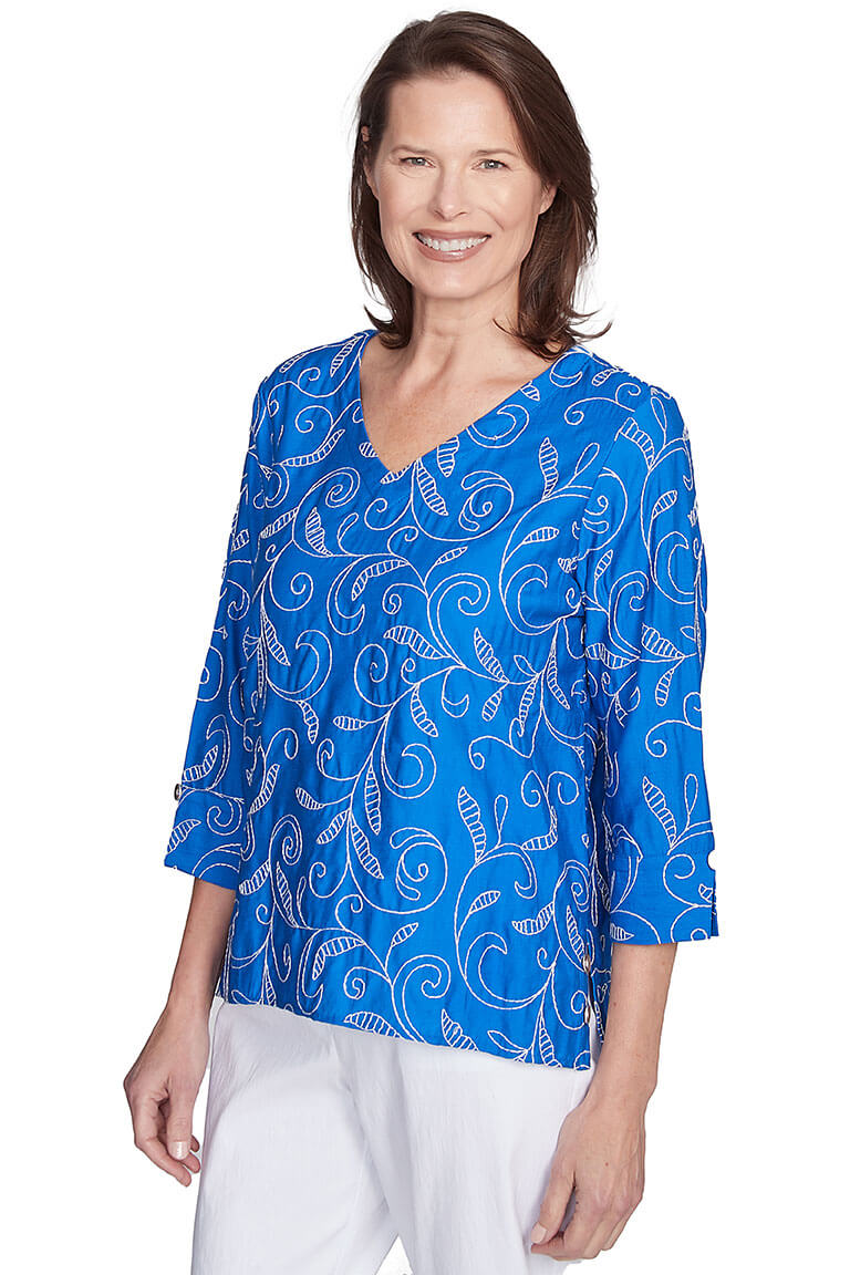 A woman wearing a blue v-neck blouse with 3/4 sleeves and all-over embroidered embellishment.