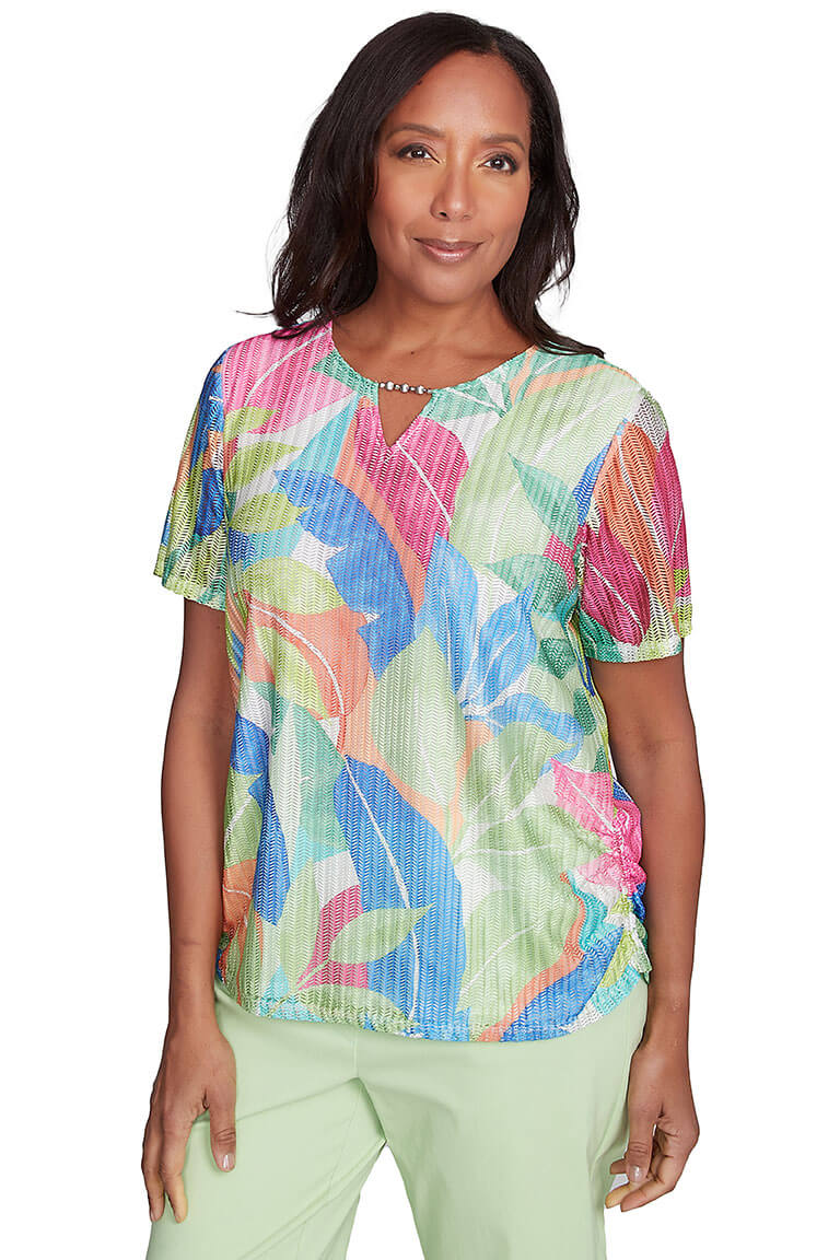 A woman wearing a multicolored tropical mesh top with a notched v-neckline and short sleeves.