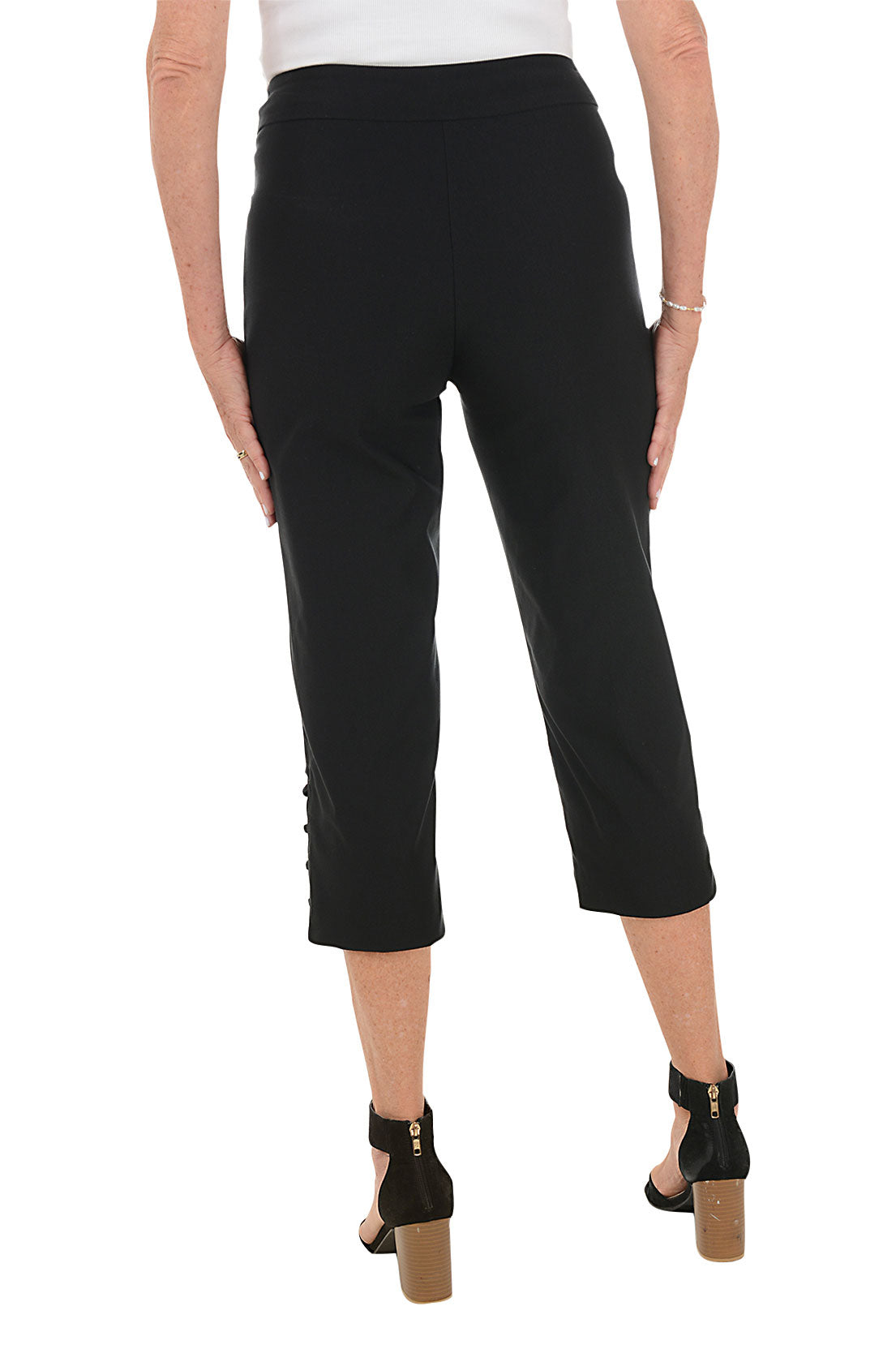 Person wearing black capri pants with lattice detail on side hem on a white background. Back shot.