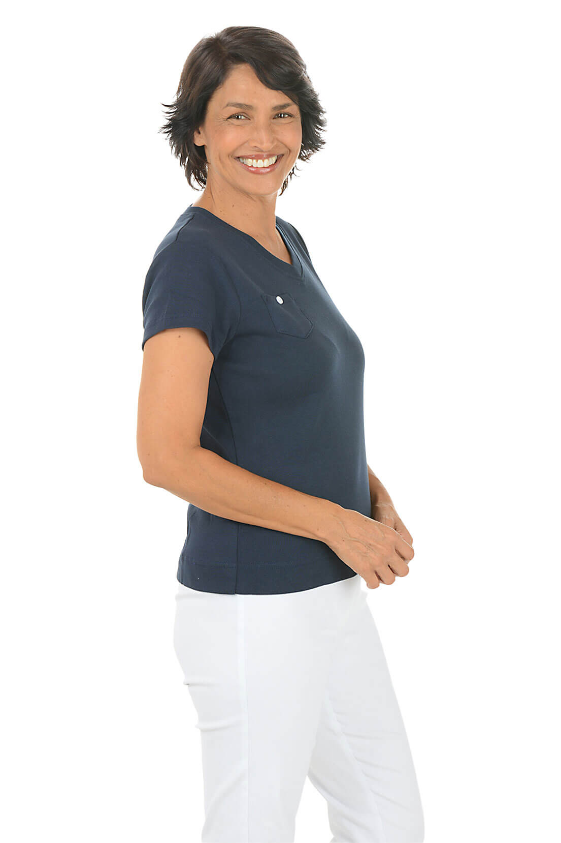 A smiling woman with short brown hair is shown in profile wearing a dark navy blue V-neck scrub top and white pants against a solid white background.