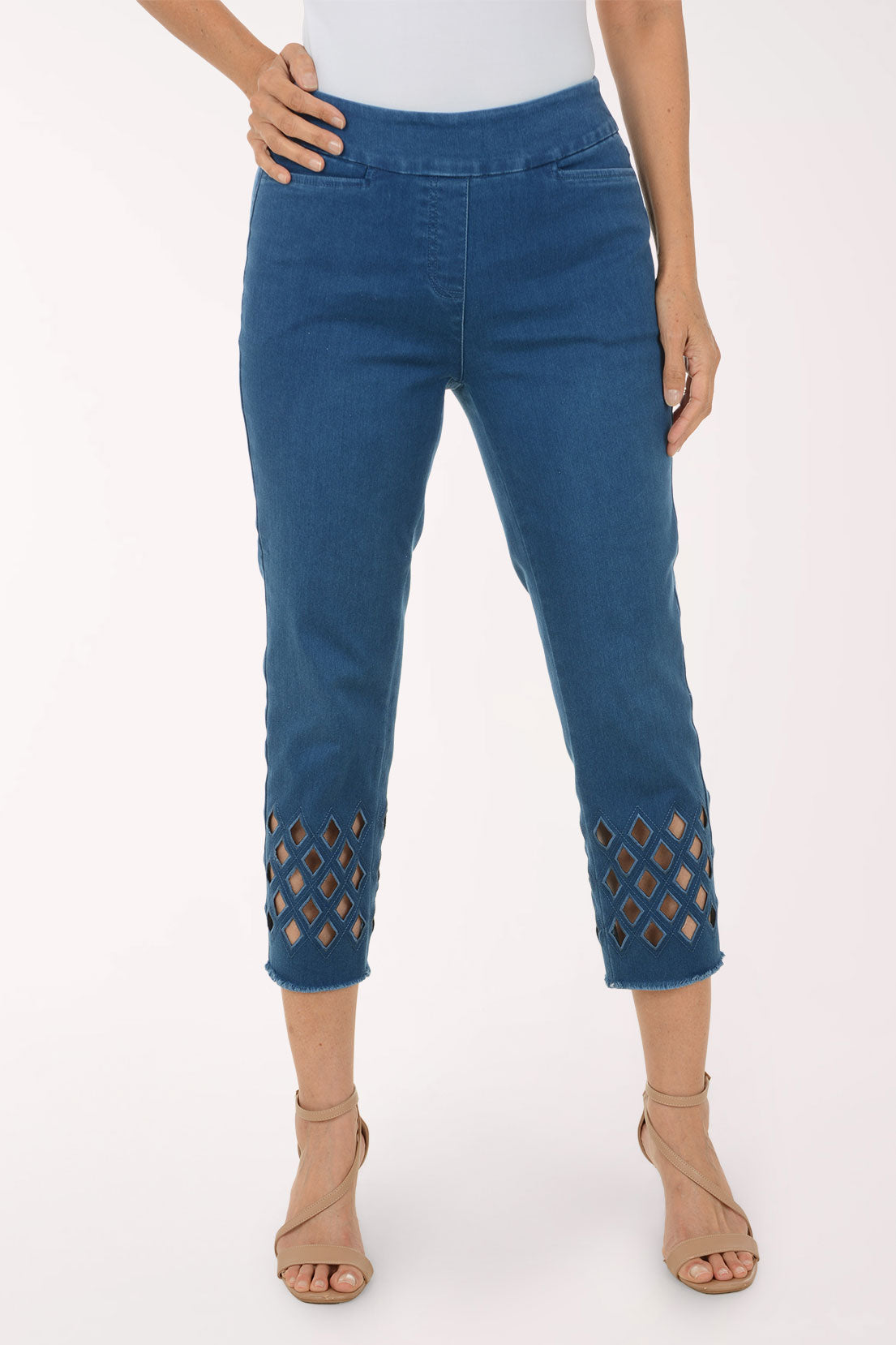 A model wearing blue cropped jeans with diamond-shaped cutout details near the hem, paired with a white top and beige strappy high-heeled sandals, against a plain white studio background.
