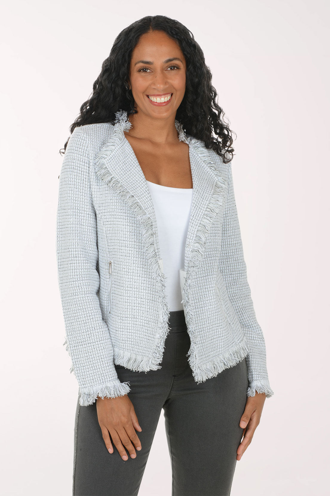 A woman modeling a light blue and white textured tweed jacket with frayed edges, worn over a white top and dark gray pants, against a plain white studio background.