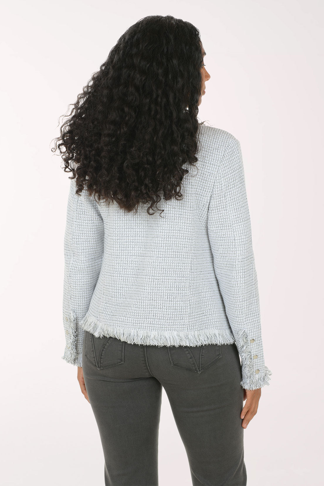 A woman modeling a light blue and white textured tweed jacket with frayed edges, worn over a white top and dark gray pants, against a plain white studio background.