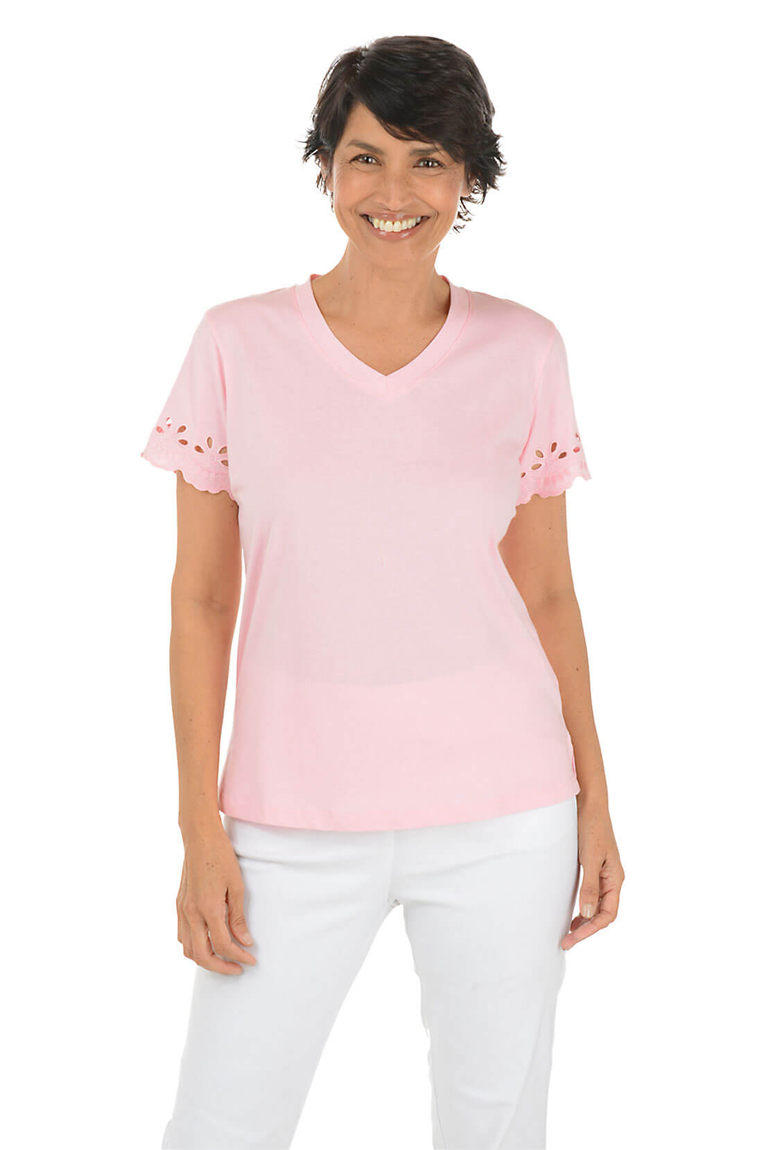 A woman wearing a light pink short-sleeved t-shirt with eyelet scallop detailing on the sleeves, paired with white pants.