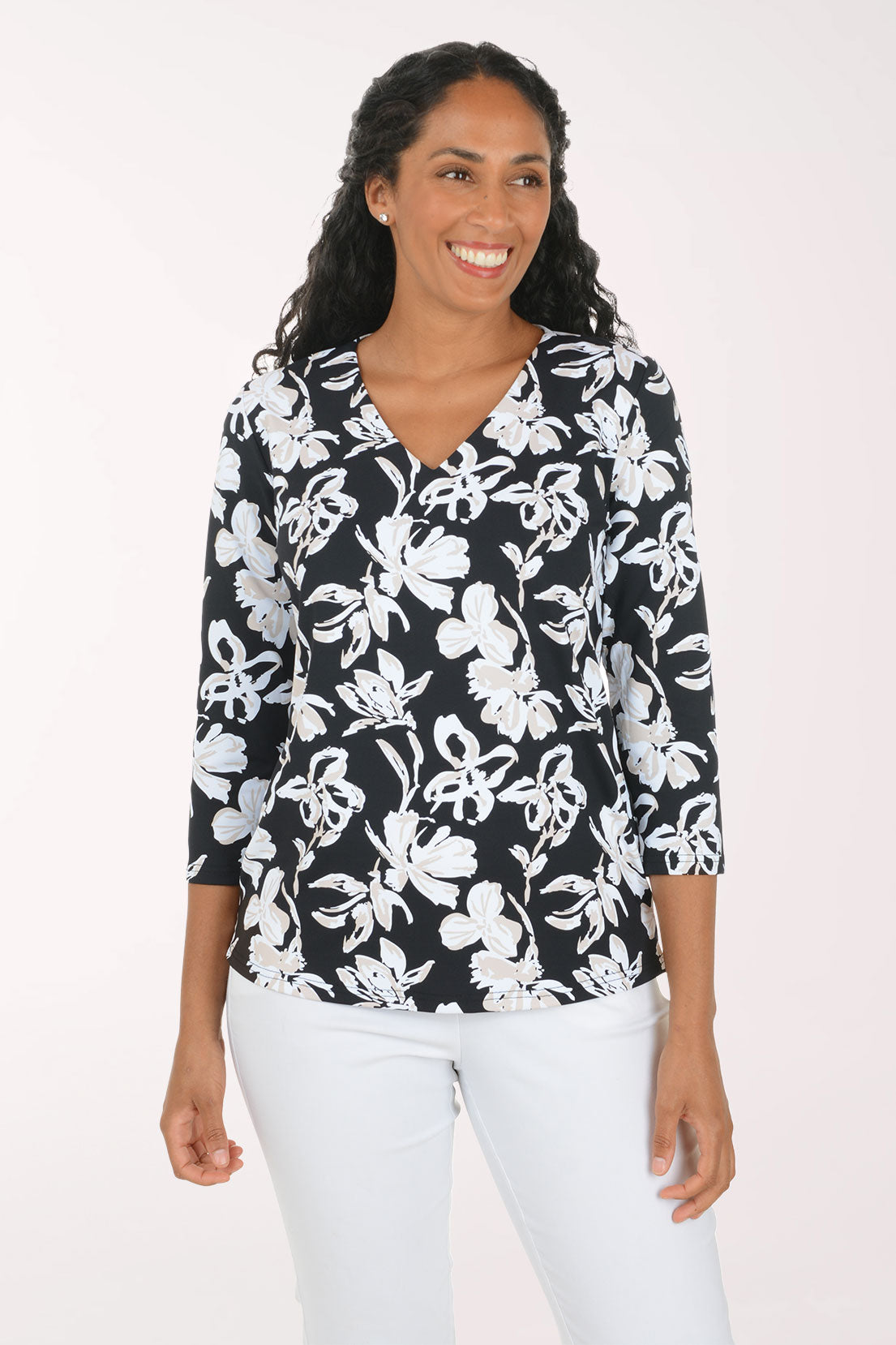 A woman modeling a black and white floral print top with three-quarter sleeves and white pants, standing against a plain light background.