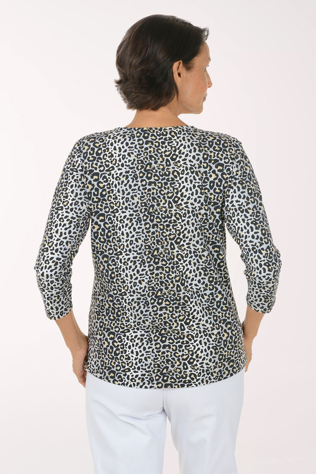 A woman modeling a black and white leopard print long-sleeve top with a V-neck, paired with white pants, against a plain light background.