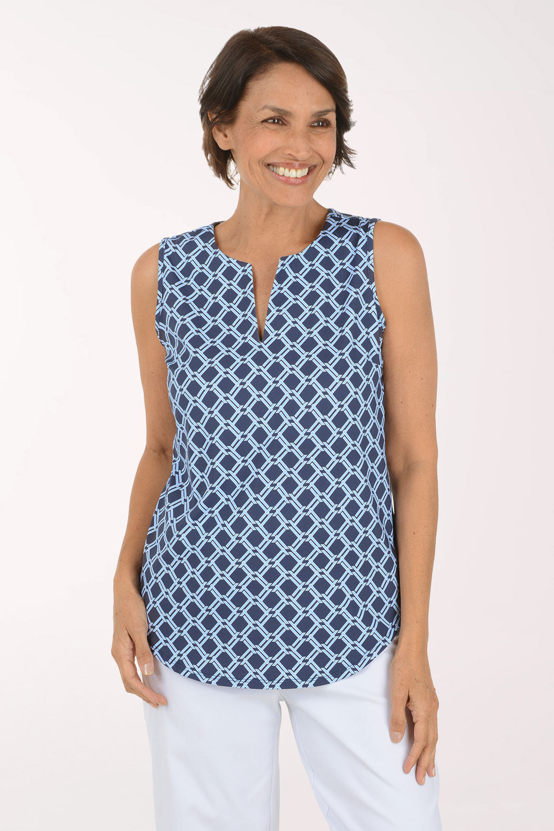 A woman modeling a sleeveless top with a navy blue and white geometric trellis pattern, featuring a split neckline and keyhole cutout, paired with white pants against a plain white studio background.