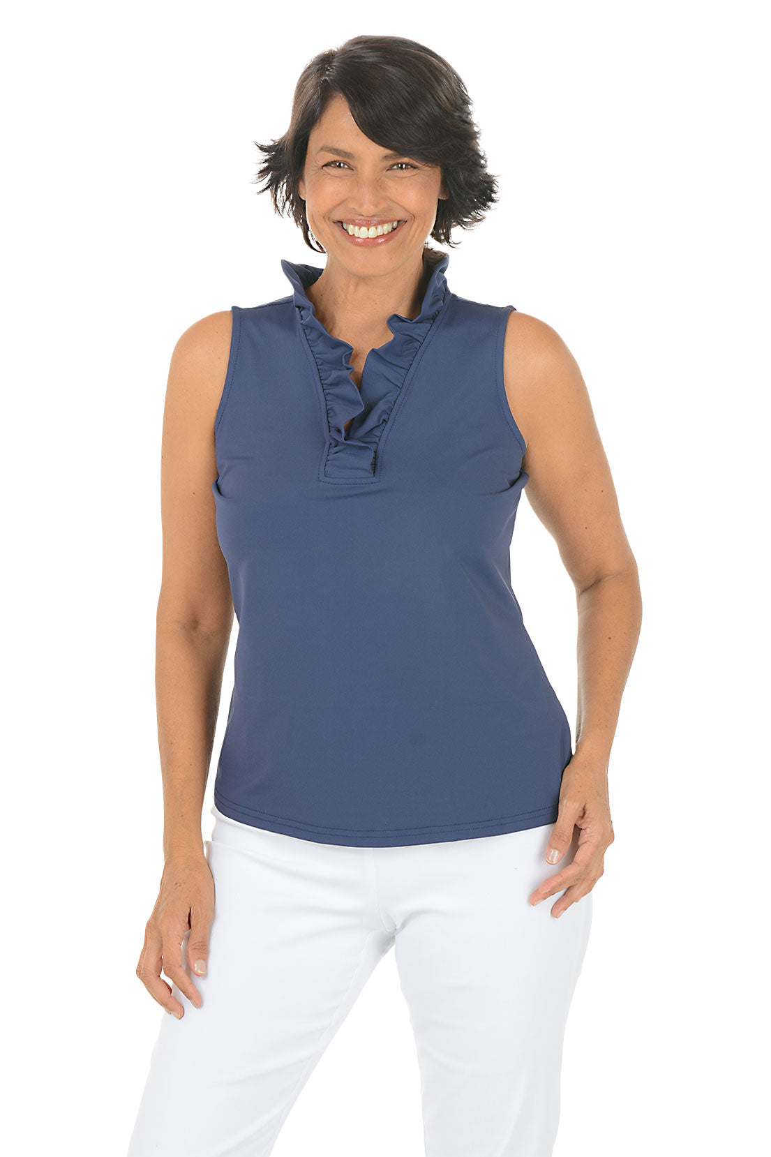 Woman wearing a navy sleeveless top with ruffles and white pants on a white background.