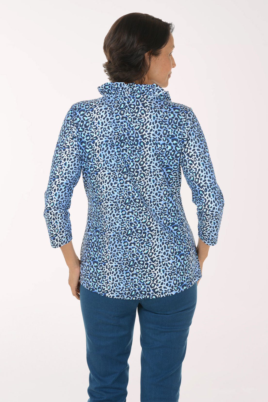 A smiling woman wearing a blue and white leopard-print button-down shirt with three-quarter sleeves and blue jeans, standing against a plain white studio background.