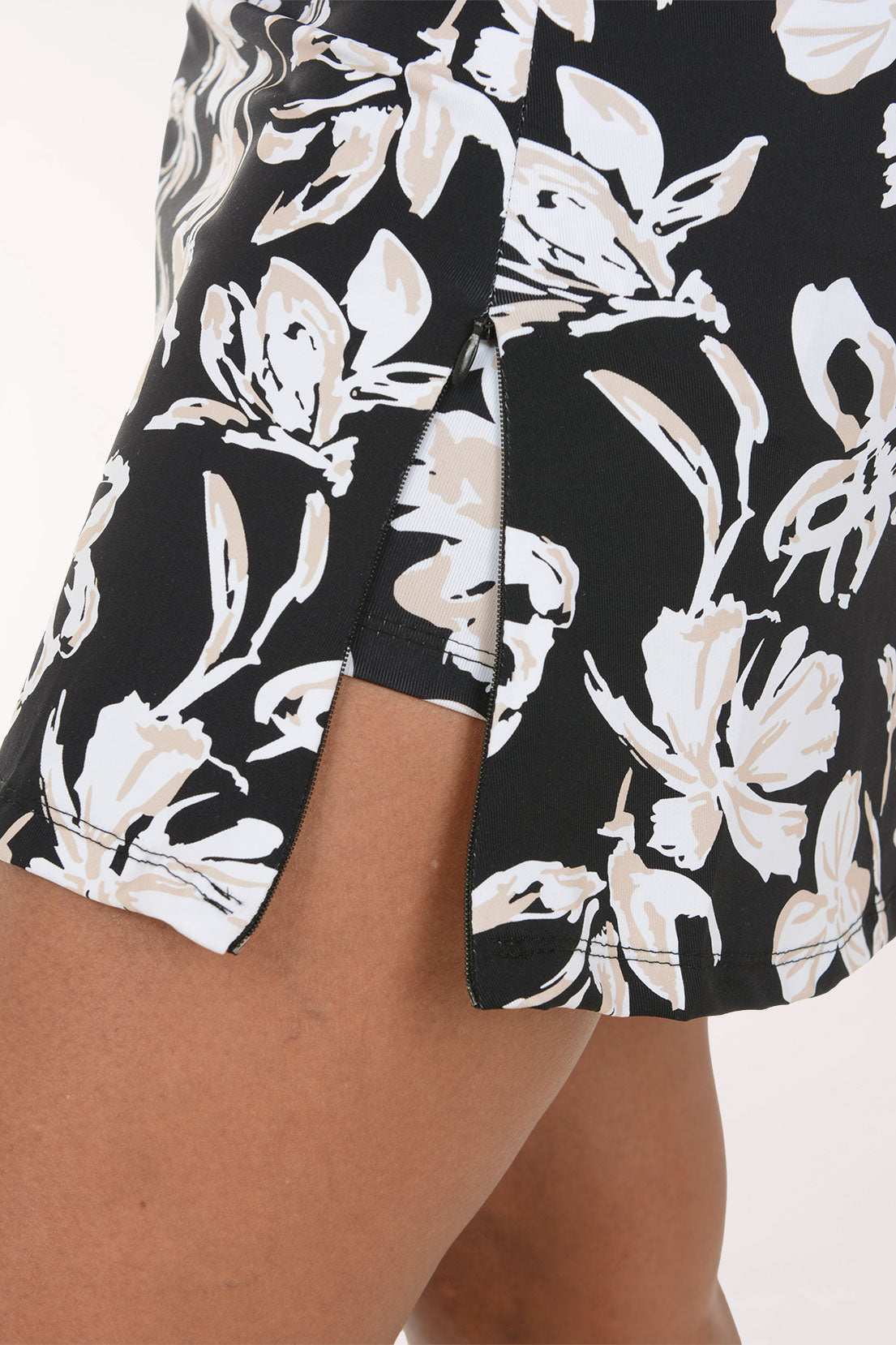 A model wearing a black and white floral print mini skirt with a white top and white sneakers, shown from the waist down against a plain white background.