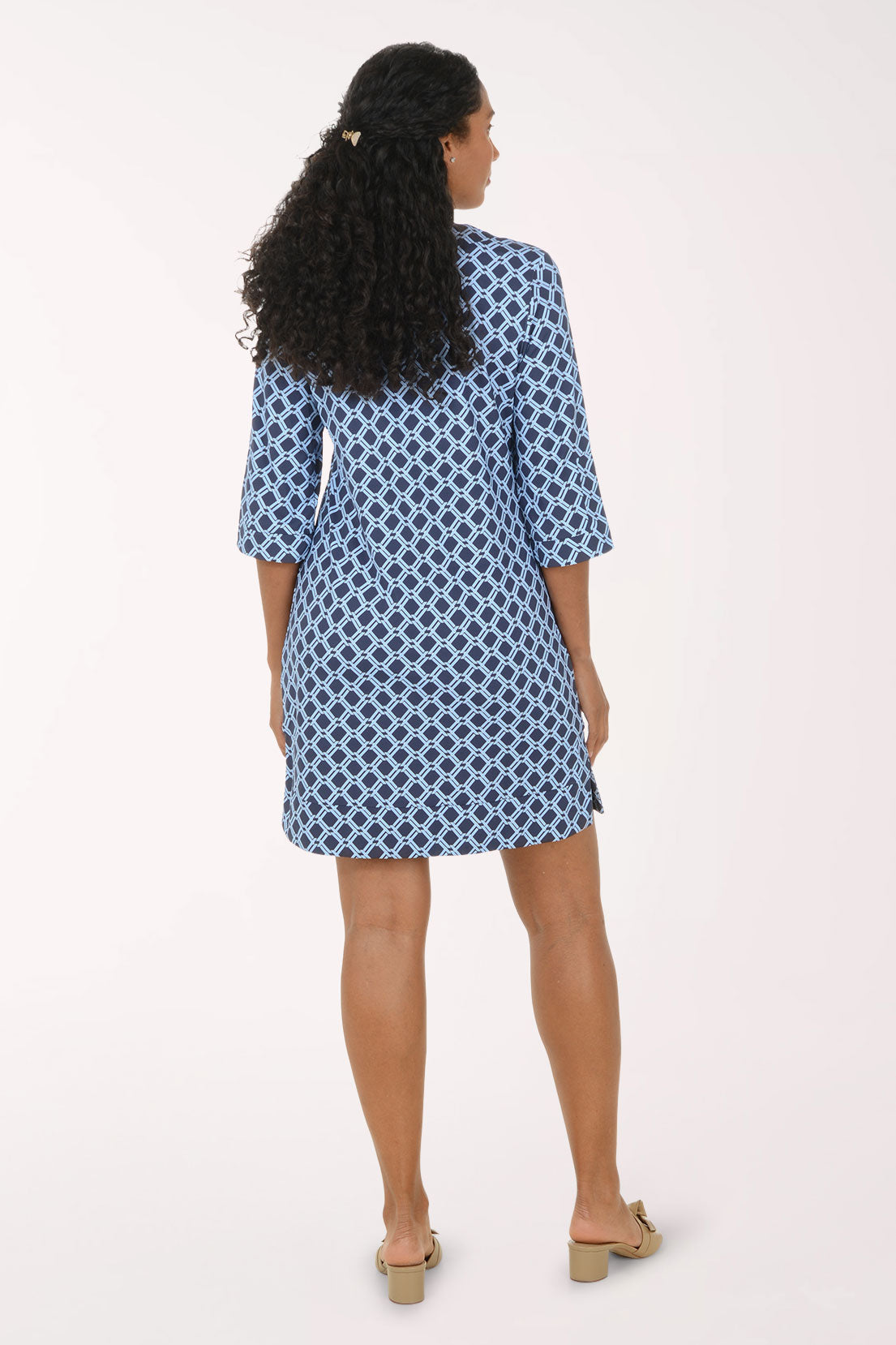 A woman modeling a short blue and white patterned tunic dress with three-quarter sleeves and a split neckline, standing against a plain light background.