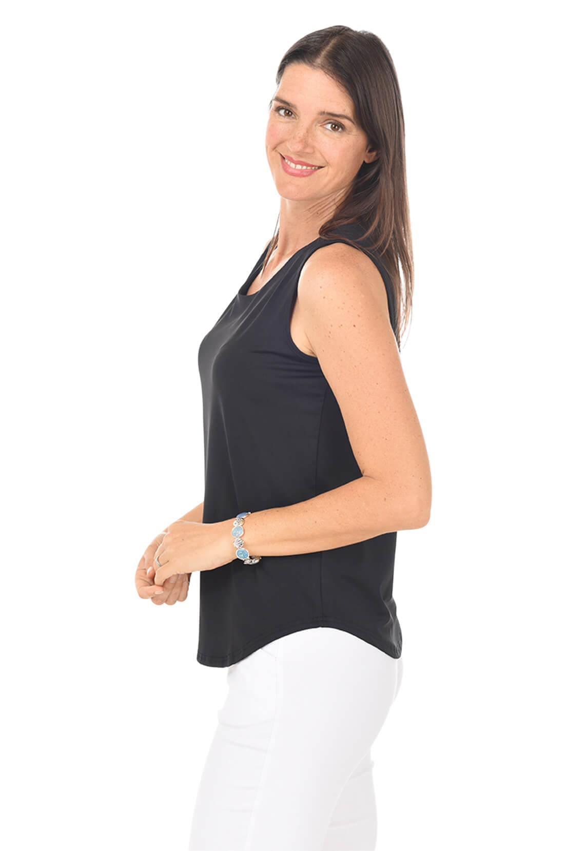 Woman wearing a black sleeveless top and white pants on a white background. Side shot.