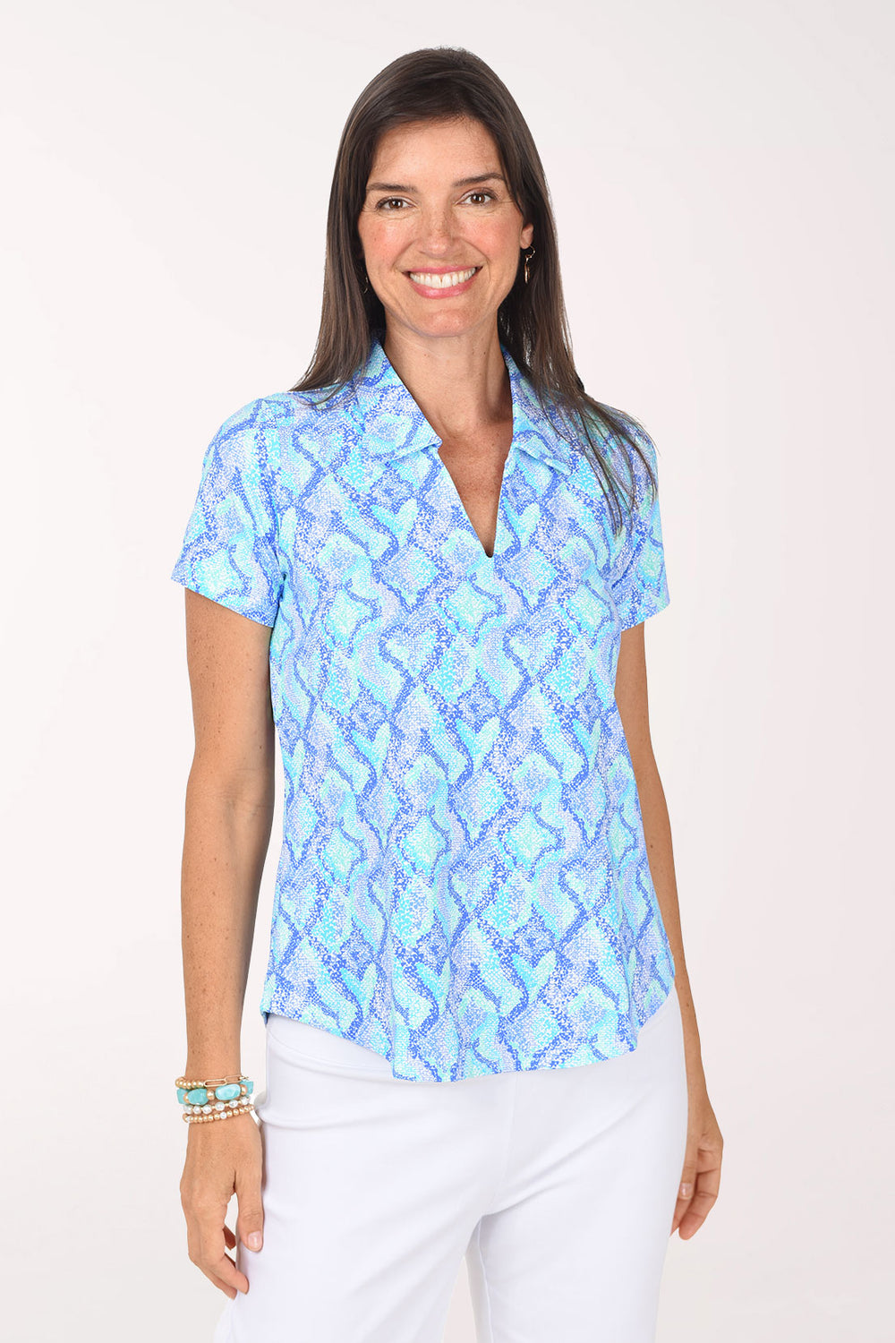 Front view of a model wearing the Anthony's Resort Wear Blue Snakeskin UPF50+ Short Sleeve Polo Top in a light blue, turquoise and periwinkle snakeskin print, with a polo collar and V-neckline, worn with white pants.