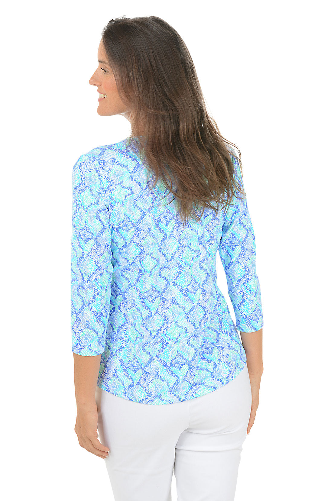 Woman wearing a blue patterned blouse with white pants on a white background. Back shot.