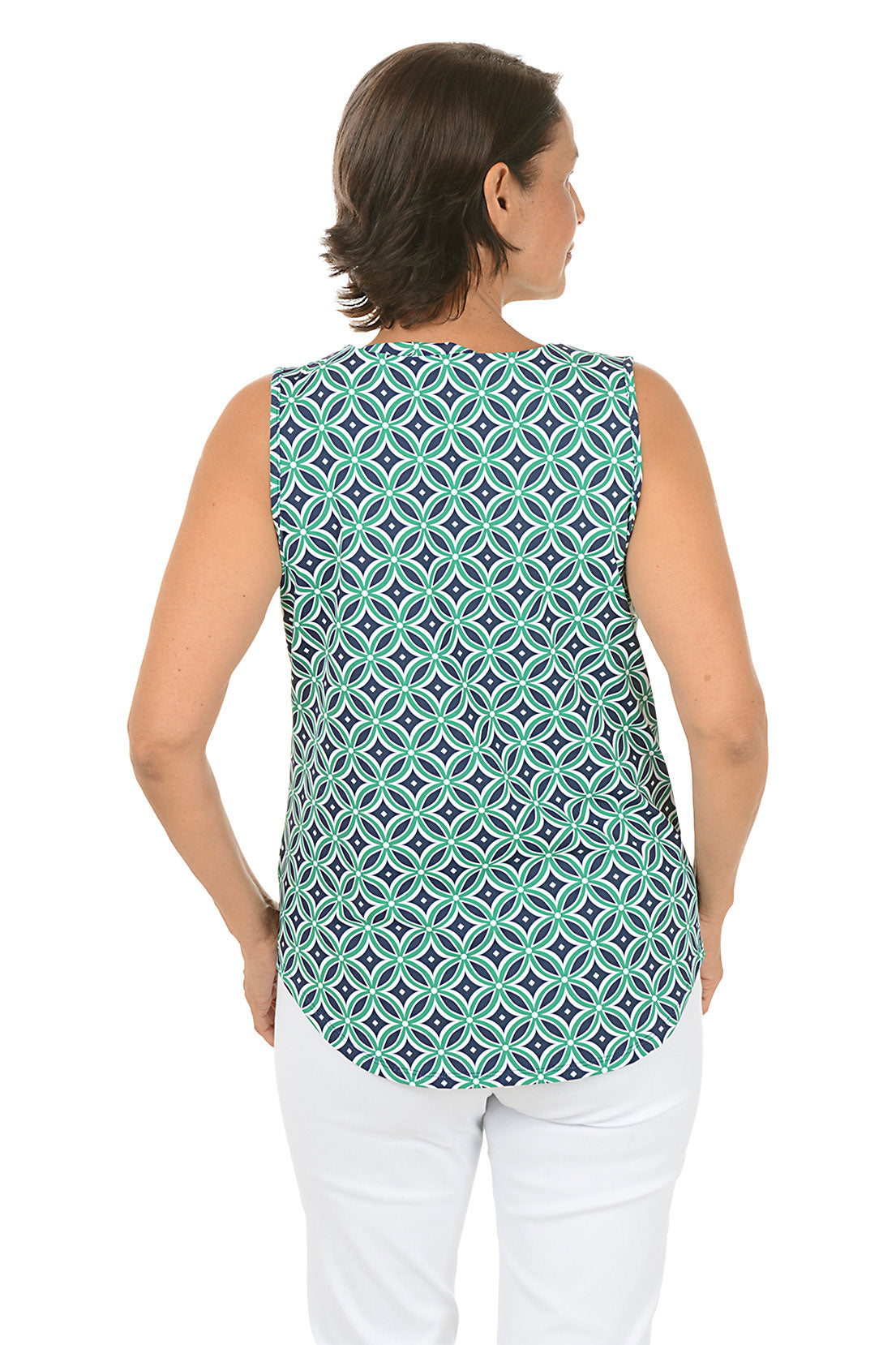Woman wearing a navy and green sleeveless patterned top and white pants on a white background. Back shot.