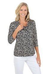 A woman wearing a 3/4 sleeve black and white giraffe pattern top with a v-neck ruffle neckline.