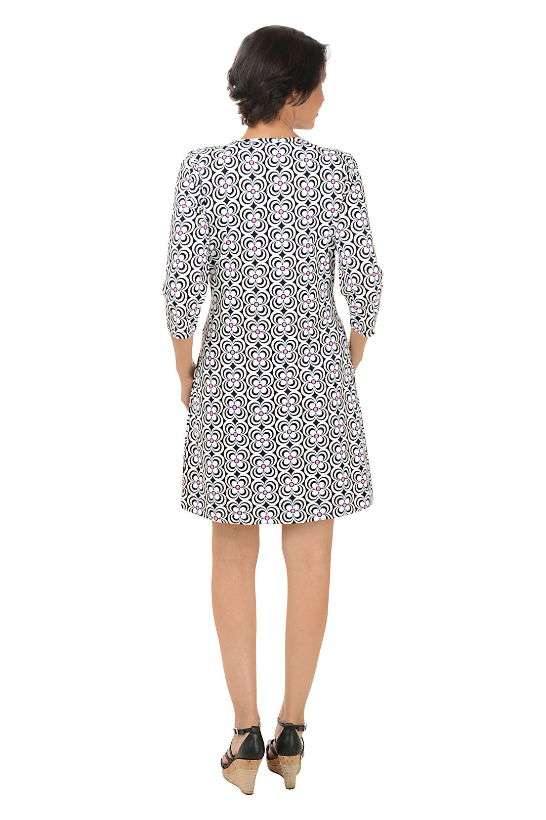A woman standing and posing in a knee-length floral dress with a scoop neckline and 3/4 sleeves. Back shot.