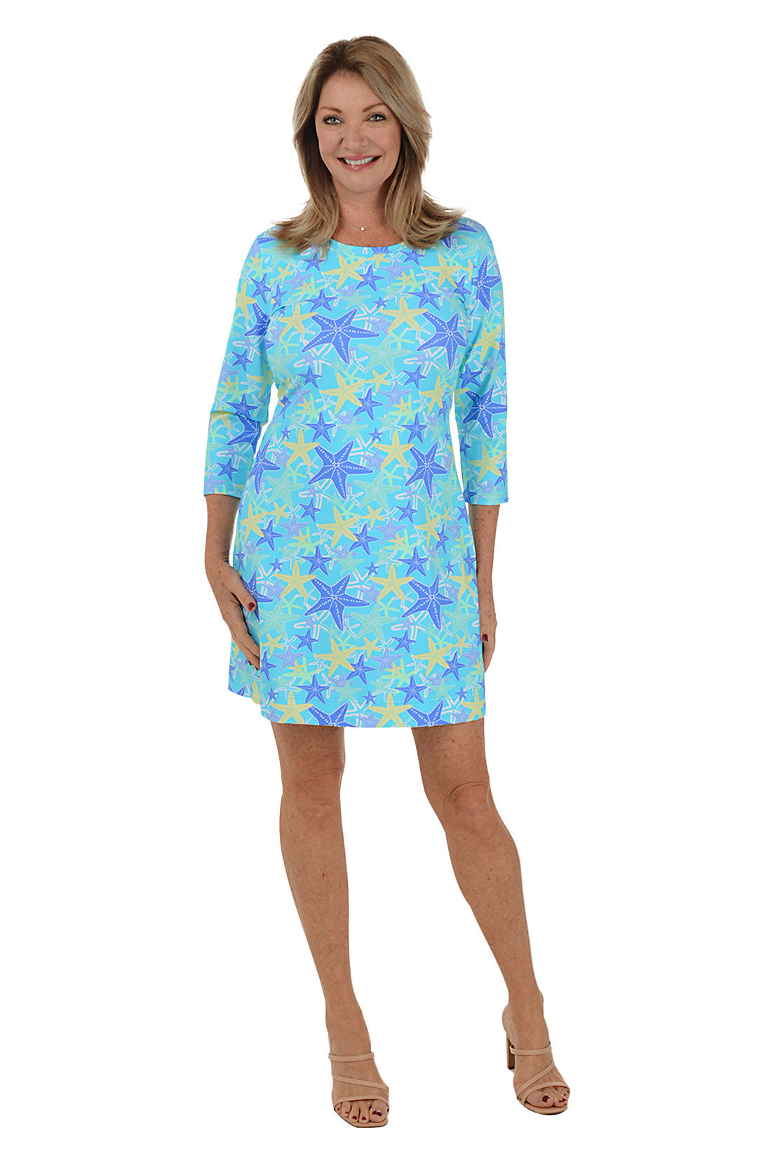 A woman wearing a 3/4 sleeved blue dress with a starfish pattern, standing against a white background. Front shot.