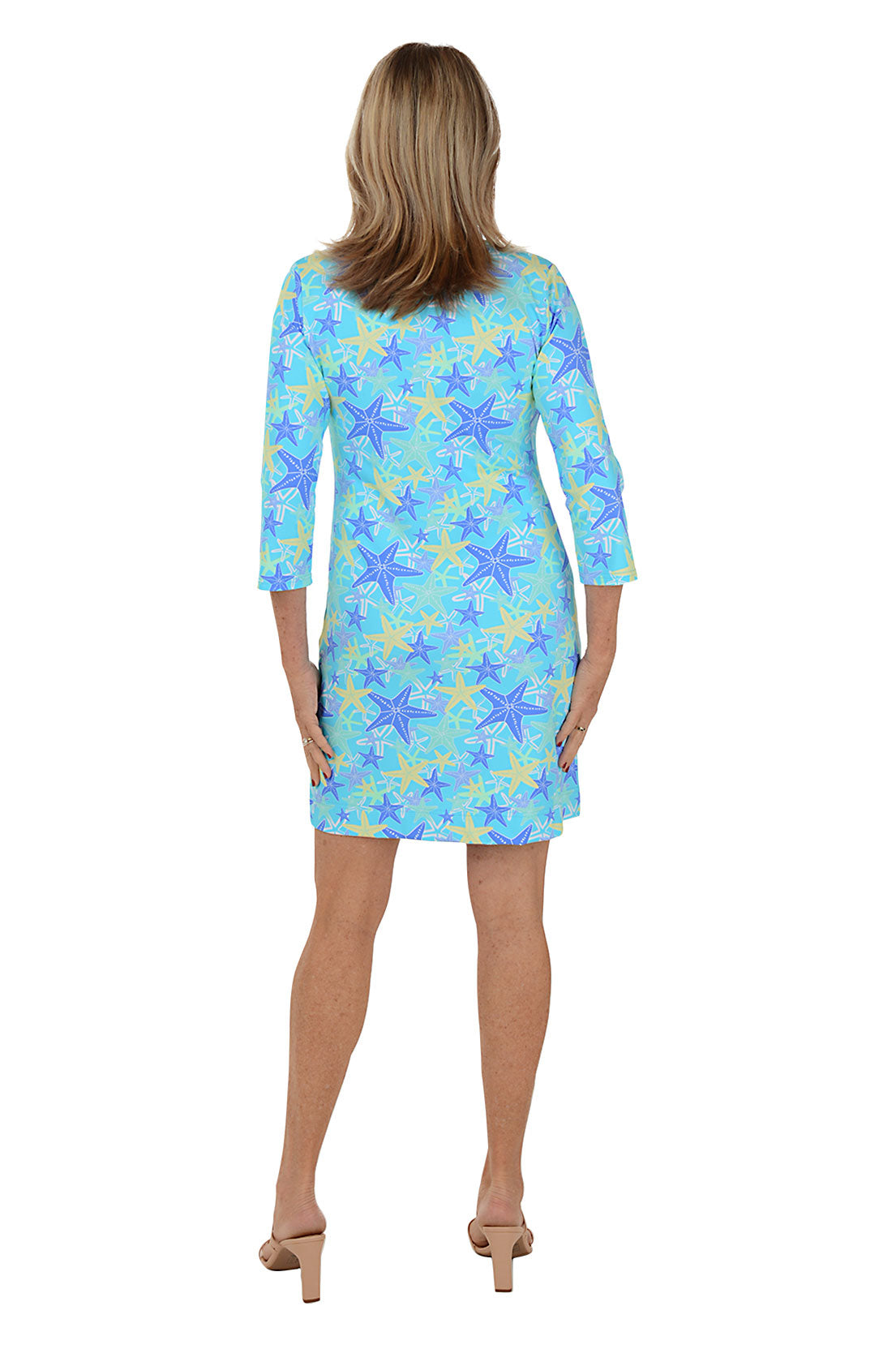 A woman wearing a 3/4 sleeved blue dress with a starfish pattern, standing against a white background. Back shot.
