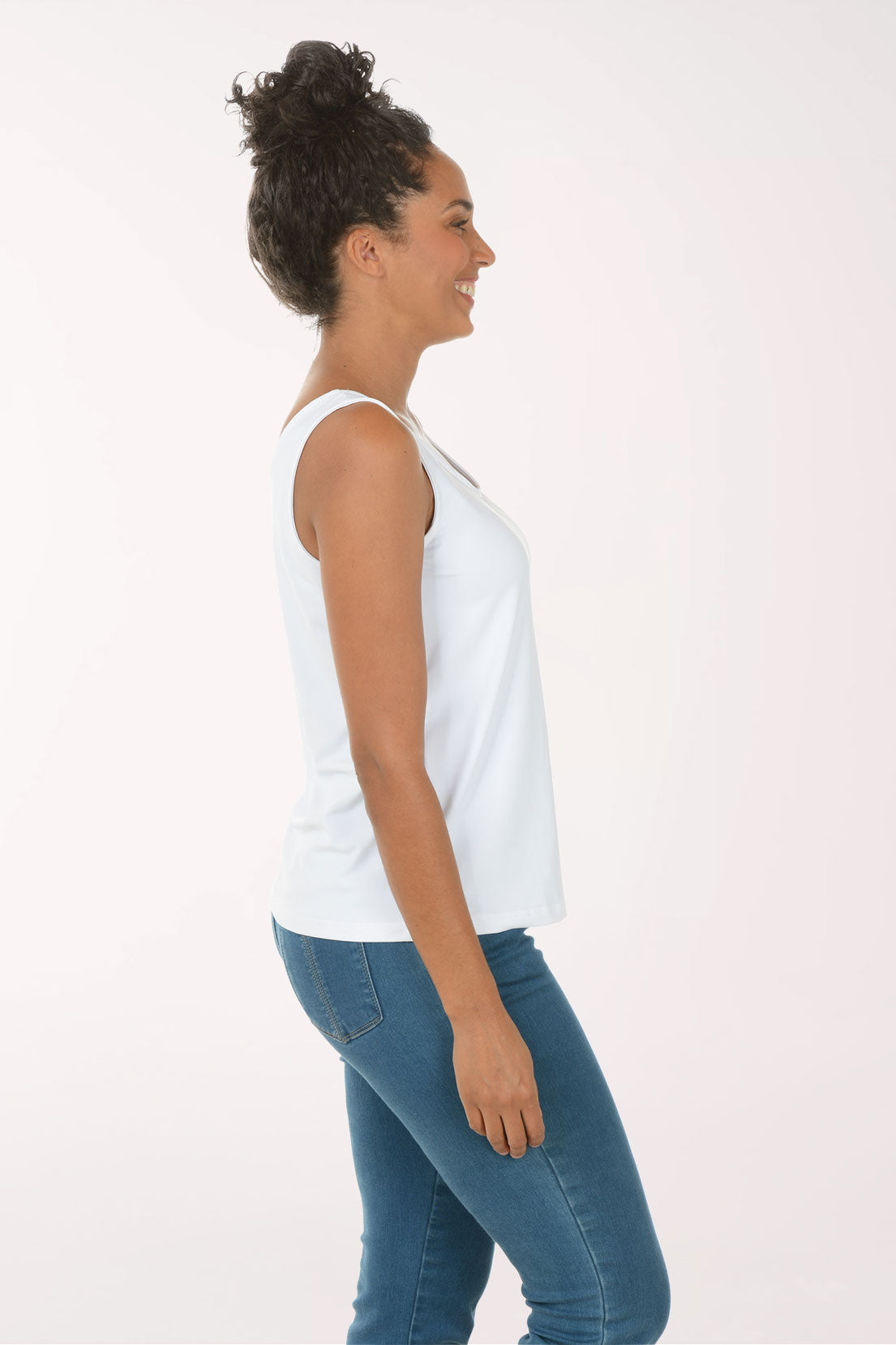 Woman wearing a white tank top and blue jeans on a white background