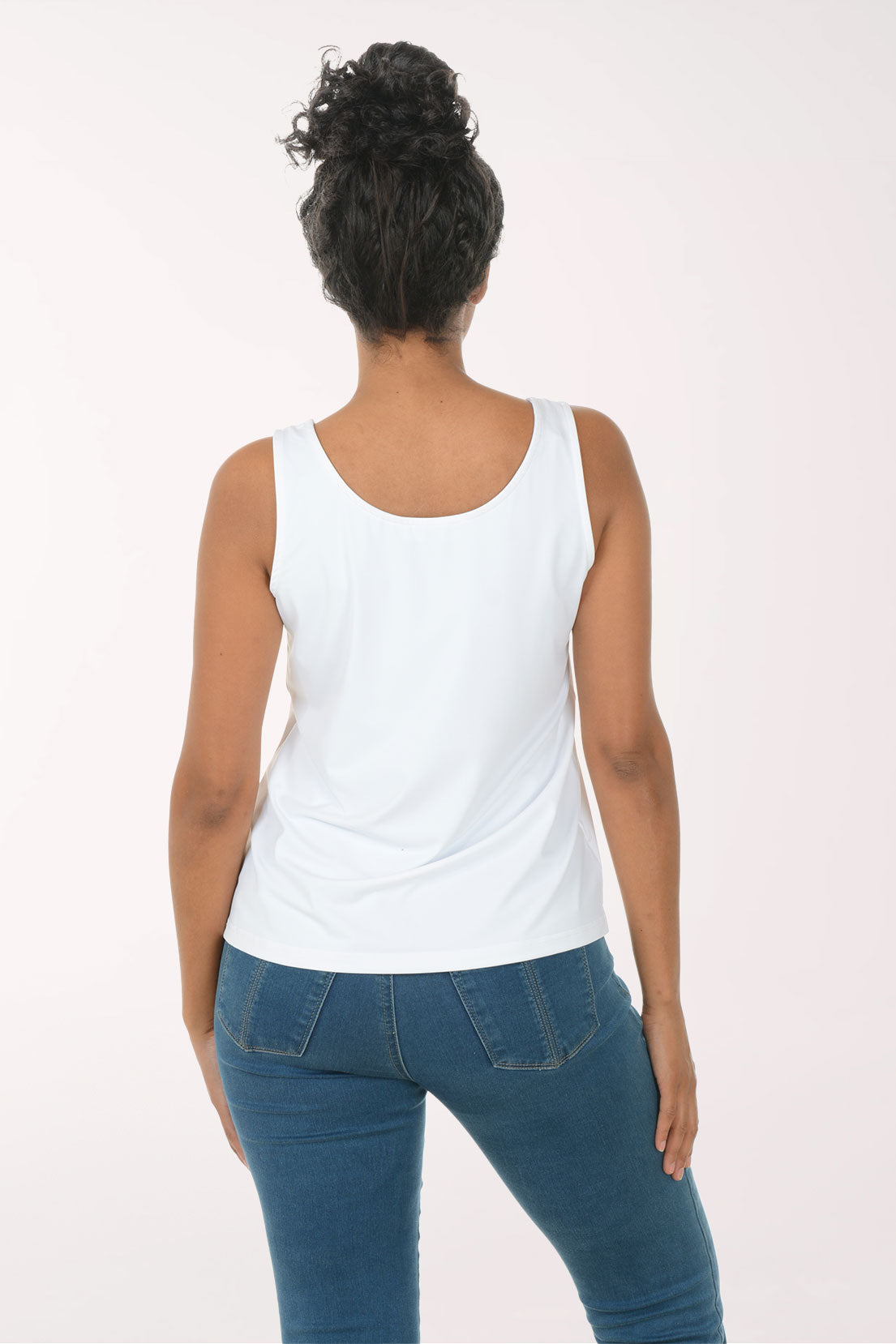 Woman wearing a white tank top and blue jeans on a white background