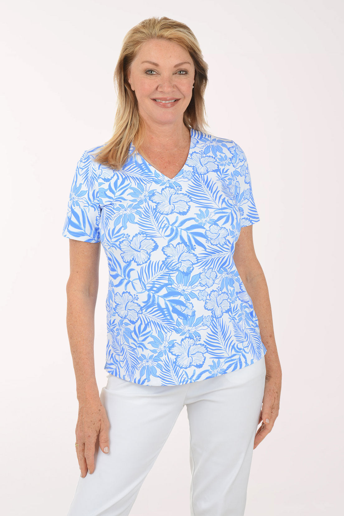 Woman wearing a blue floral patterned shirt and white pants on a white background