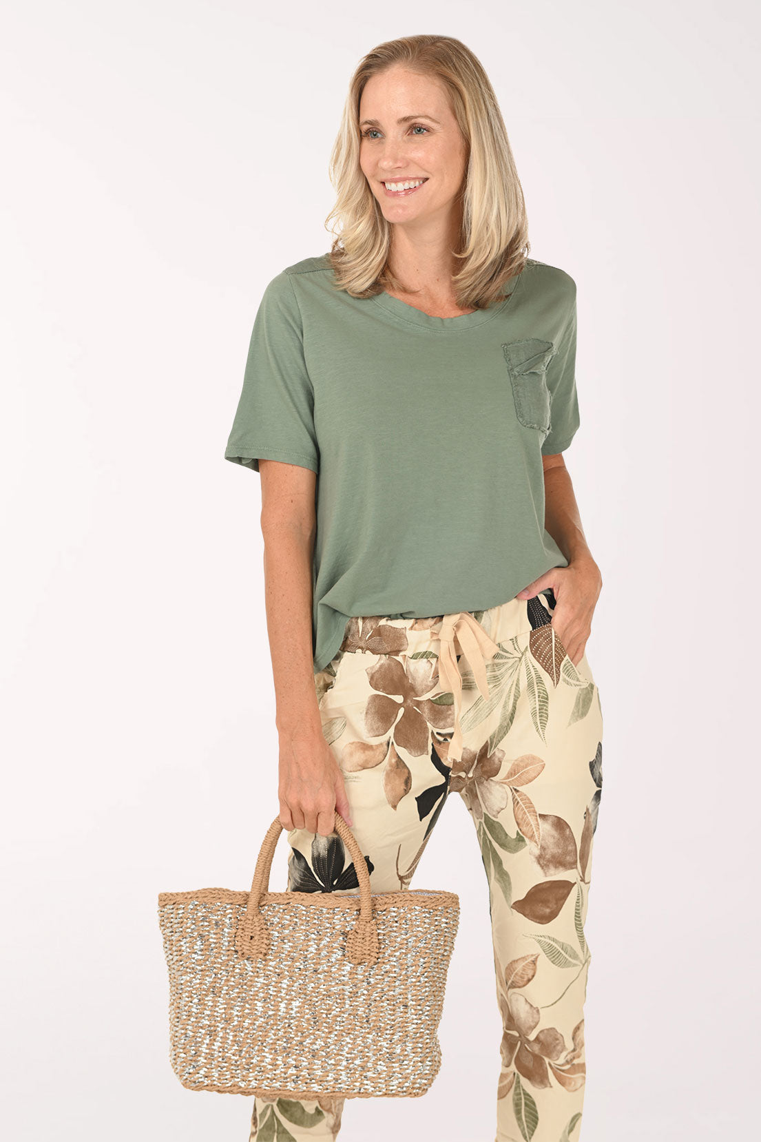 Woman wearing a green t-shirt with a pocket and floral pants on a white background