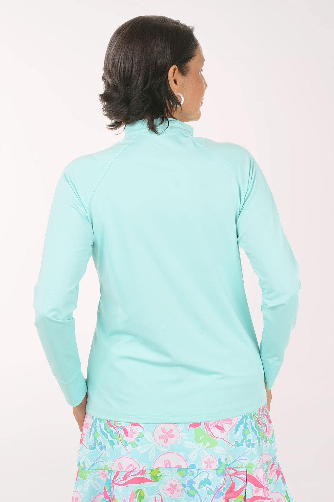 Woman wearing a light blue long-sleeve top and colorful floral skirt on a white background
